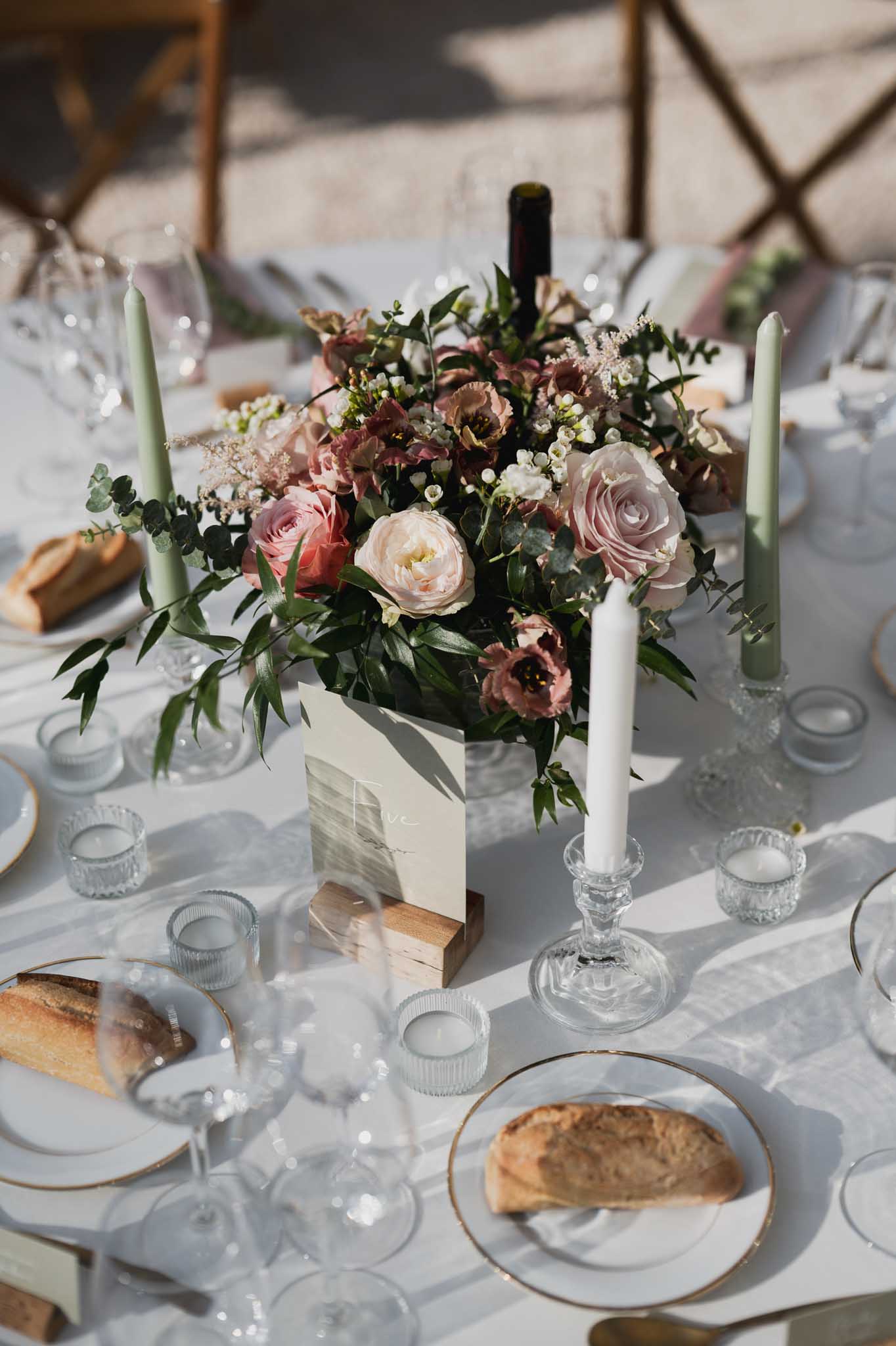 Wedding reception table setting with floral centerpiece and gold-rimmed plates at outdoor venue
