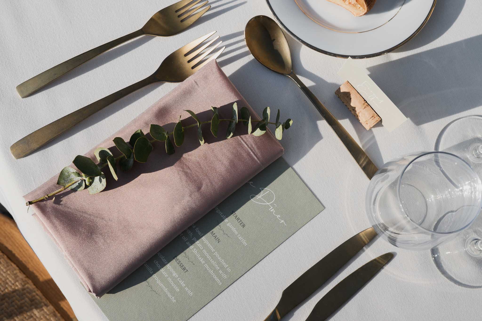 Elegant table setting with dusty rose napkin, sage menu card, and gold flatware for wedding reception