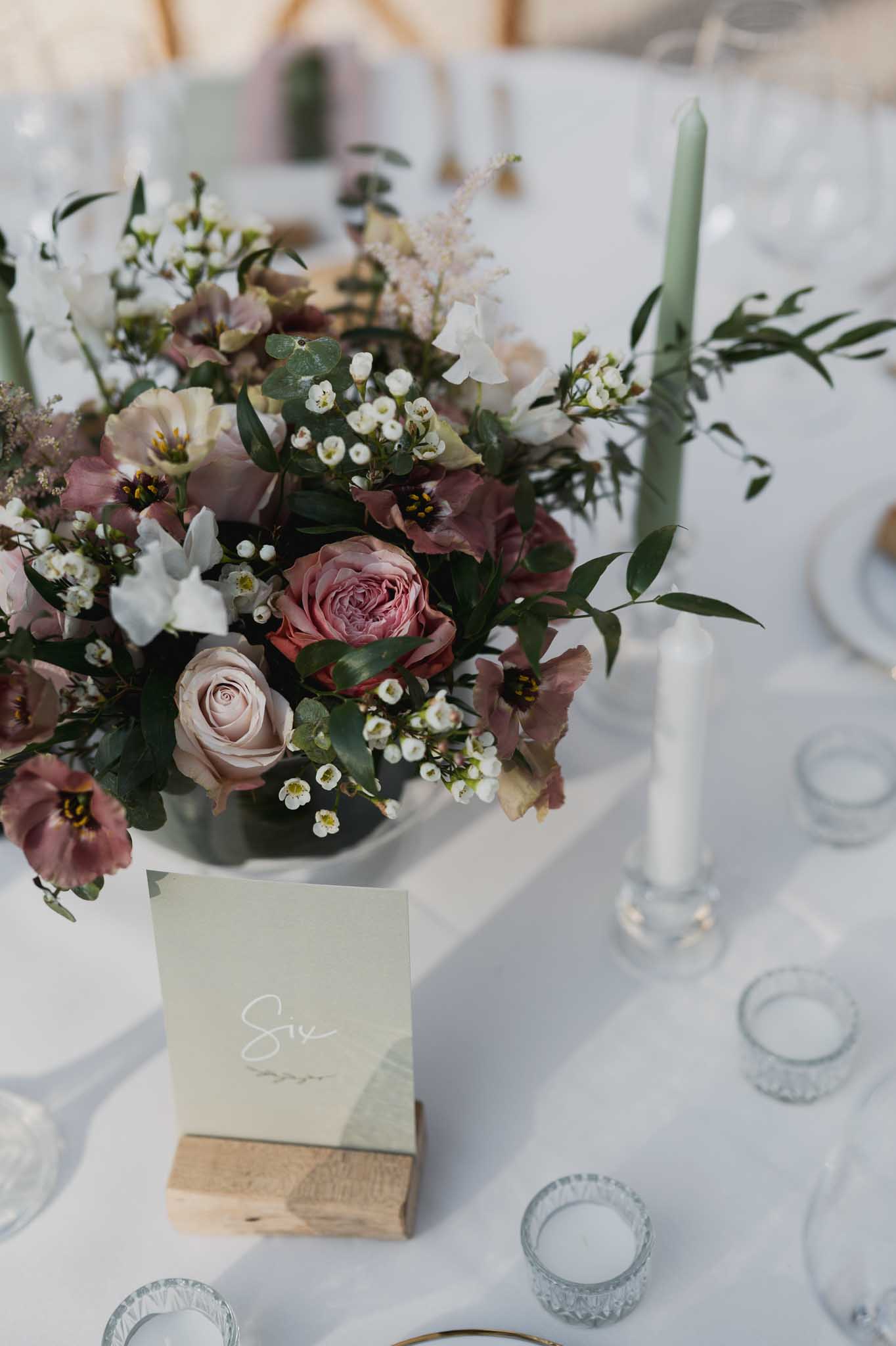Floral centerpiece with mauve roses and burgundy ranunculus on reception table with sage candle and place card