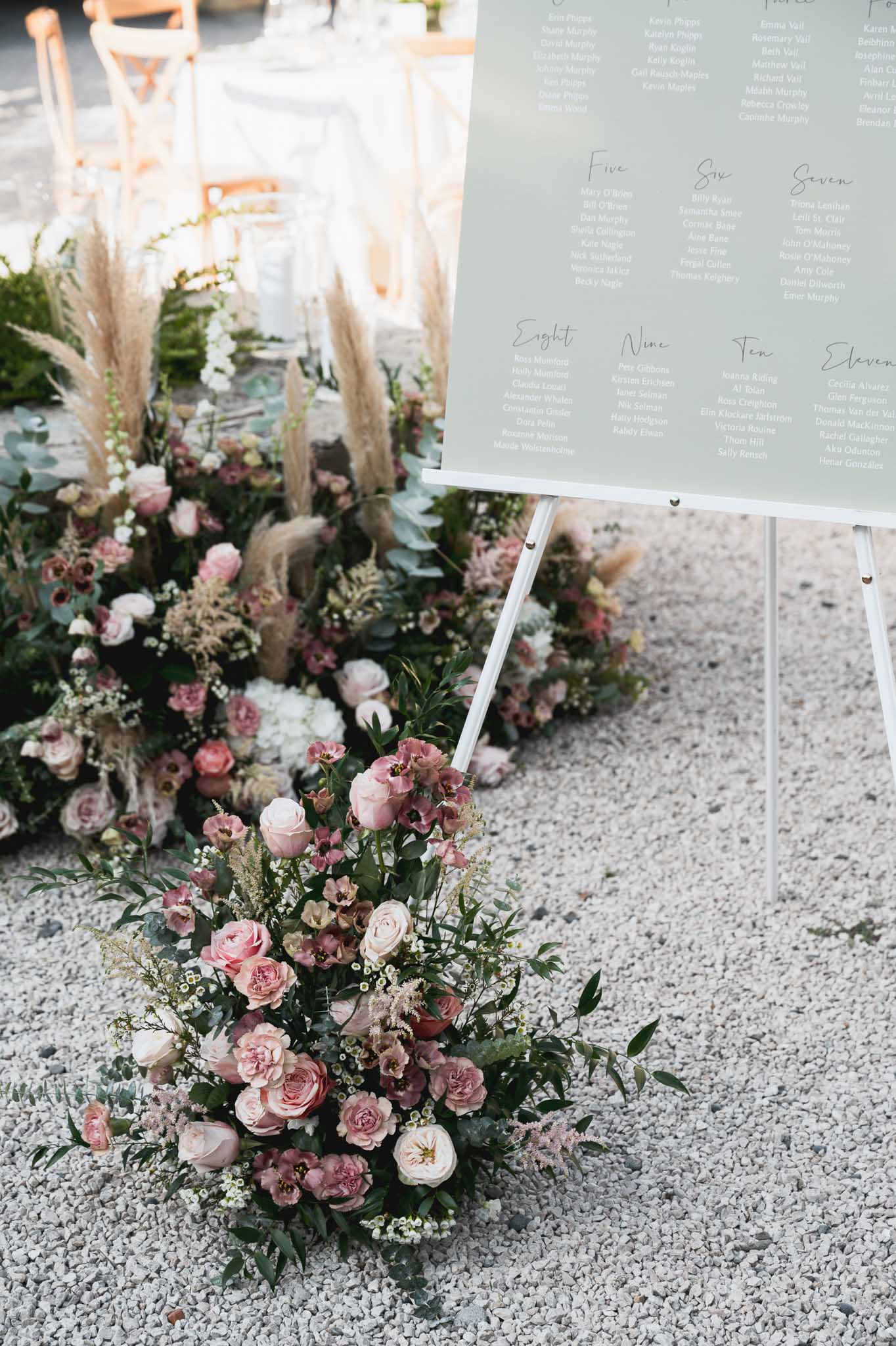 Sage green seating chart display with pink and ivory floral arrangements at outdoor wedding reception