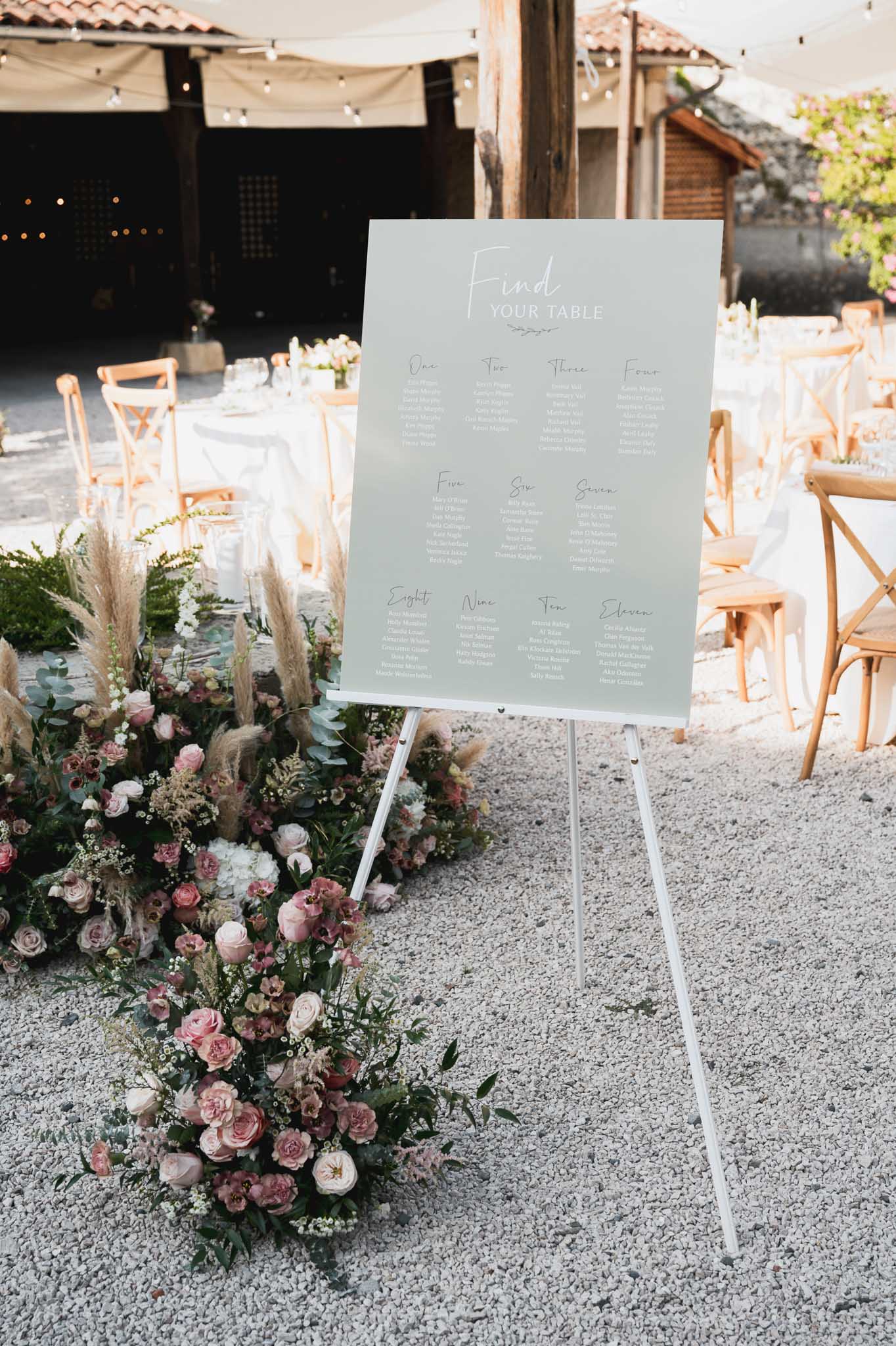 Wedding seating chart display with floral arrangement at outdoor courtyard reception entrance