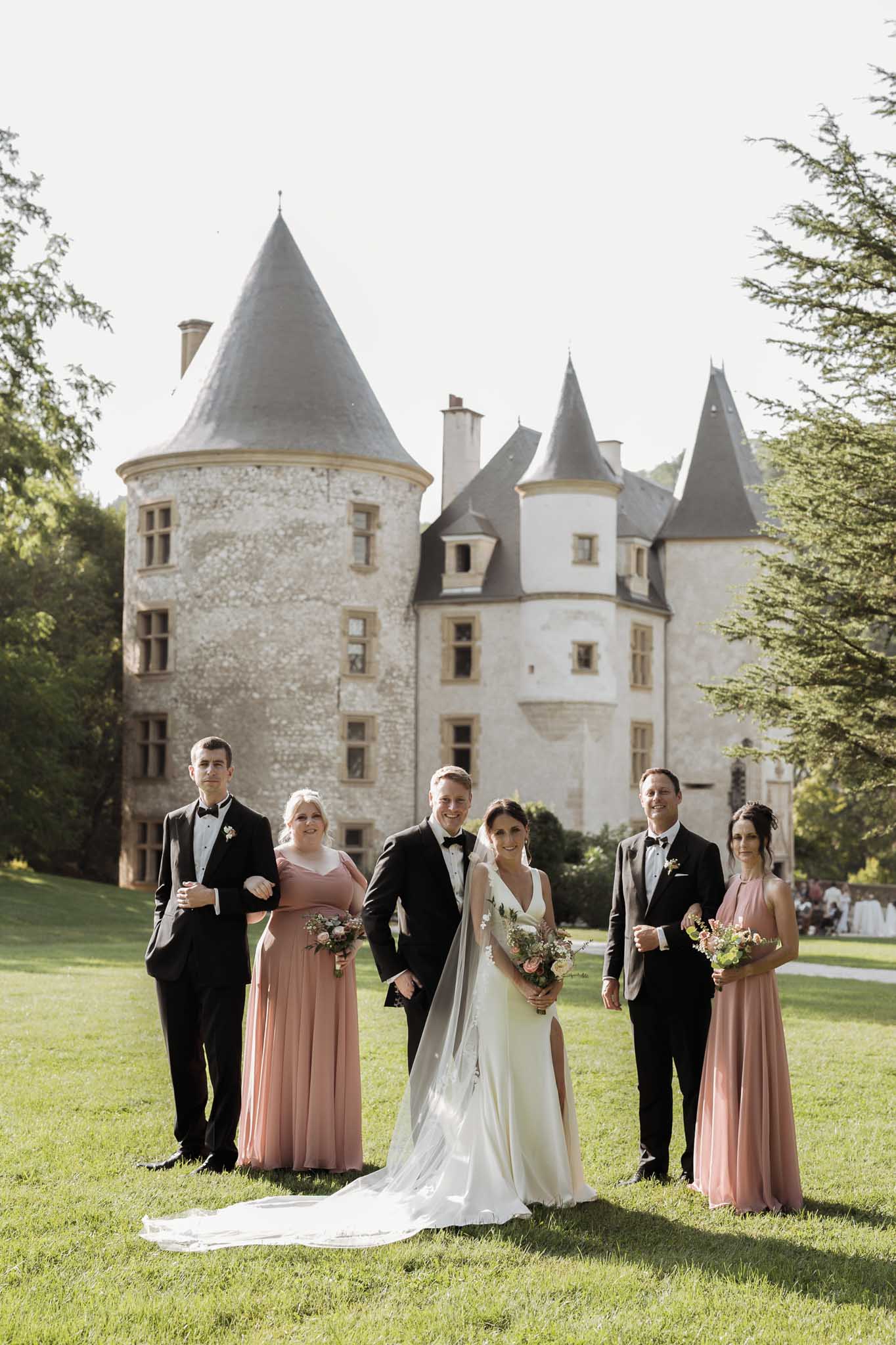Bridal party portrait with bride, groom and wedding party on lawn in front of stone château with turrets