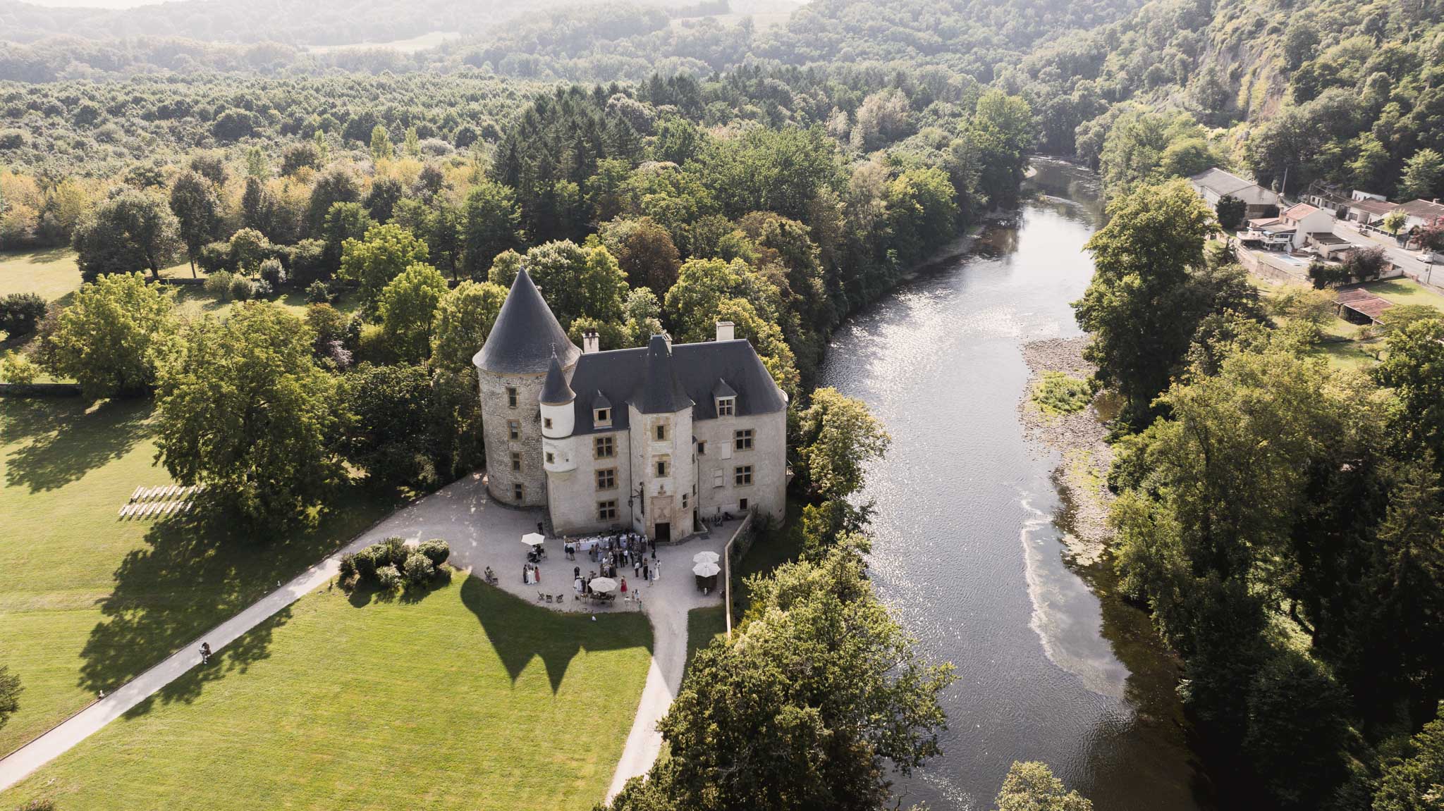 Aerial view of medieval castle wedding venue with conical tower surrounded by forested hills and river