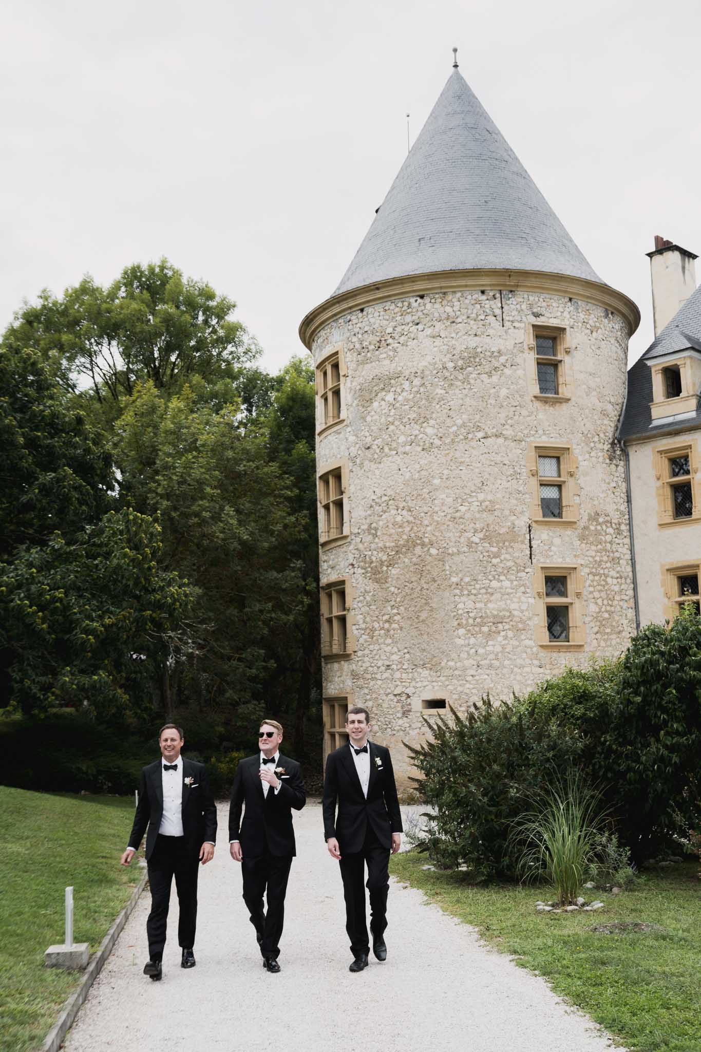 Groom and groomsmen in black tuxedos walking at historic château courtyard