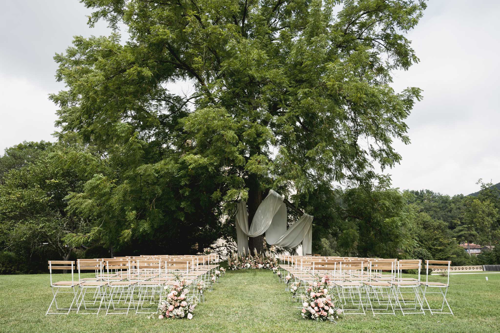 Outdoor wedding ceremony setup with draped tree canopy and floral arrangements on garden lawn