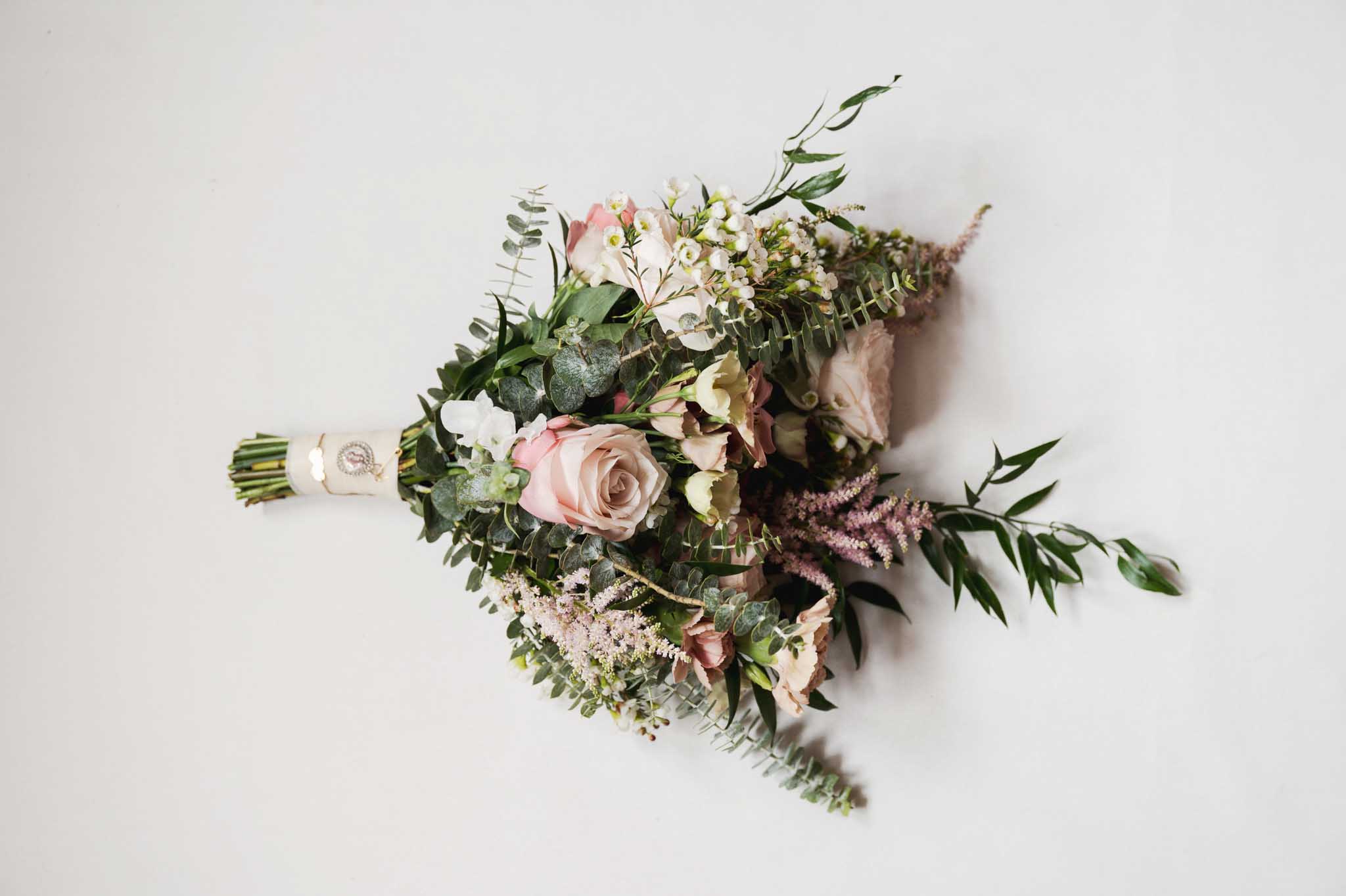 Bridal bouquet with blush roses and greenery photographed from above on white background
