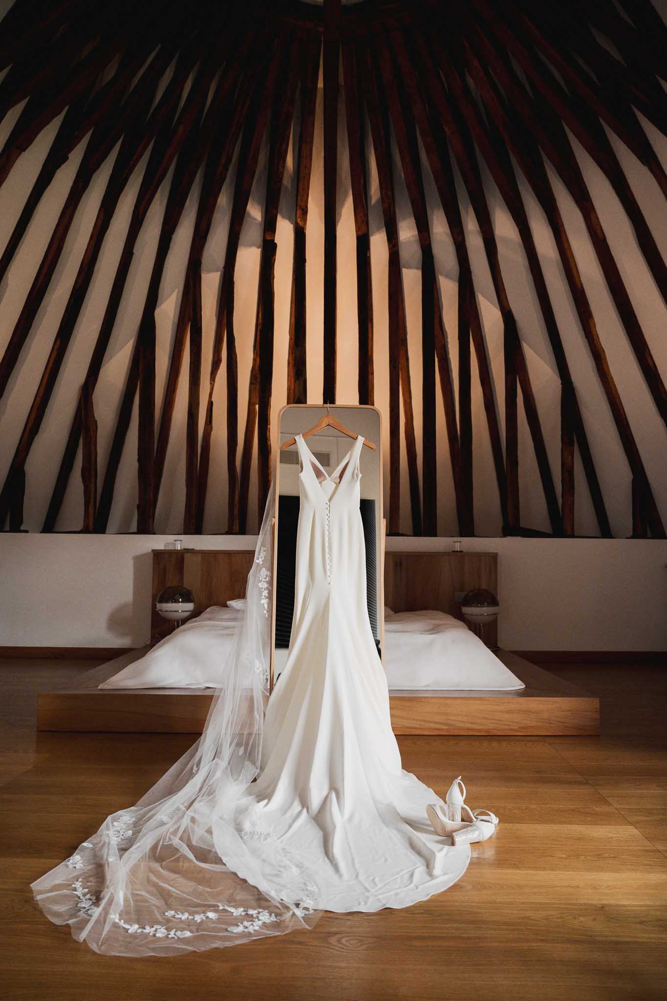 Ivory wedding gown hanging in modern bedroom with vaulted ceiling and wooden beams