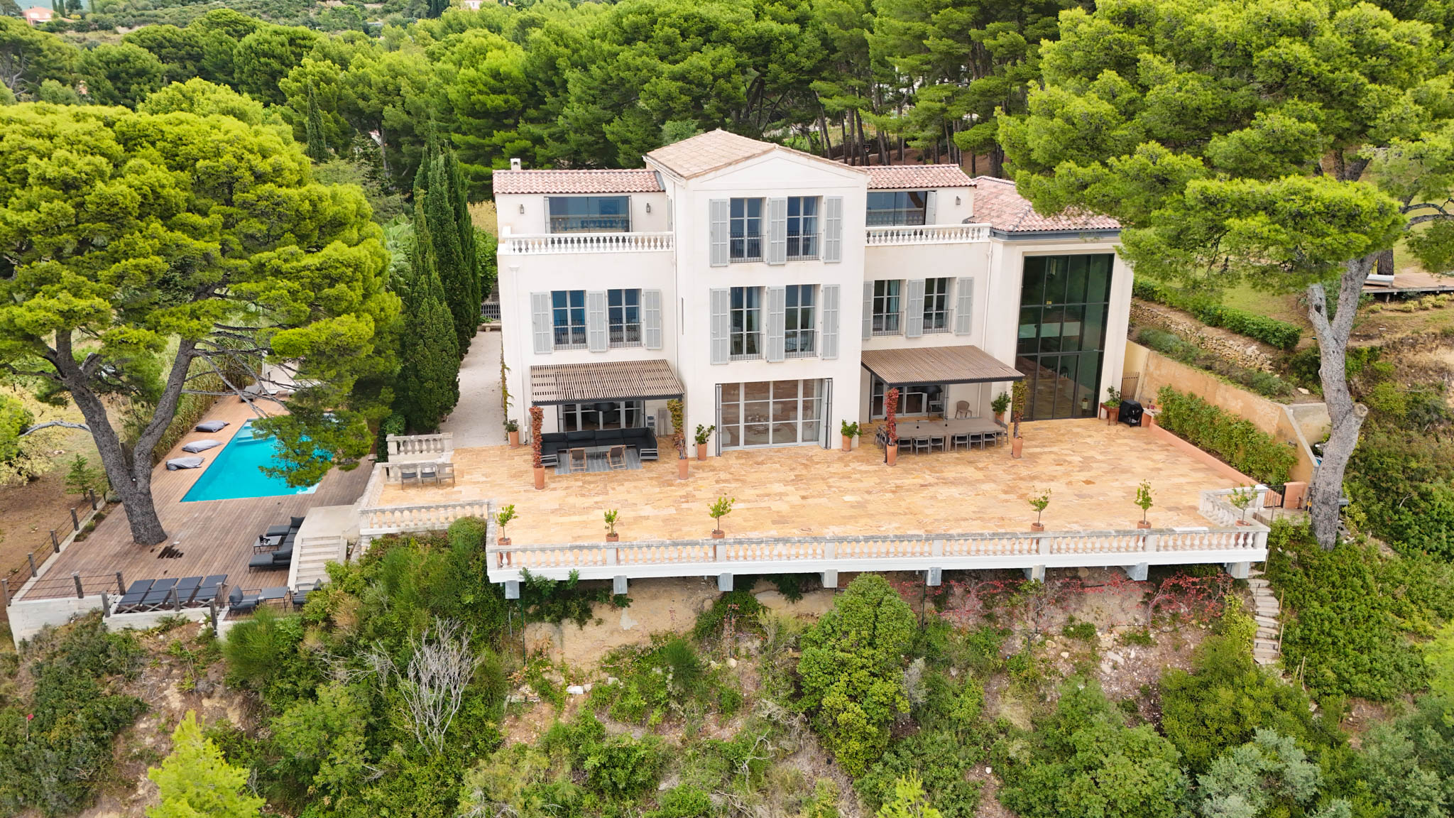 Aerial view of white Provencal villa with terracotta roof, stone terrace, pergolas, and turquoise pool