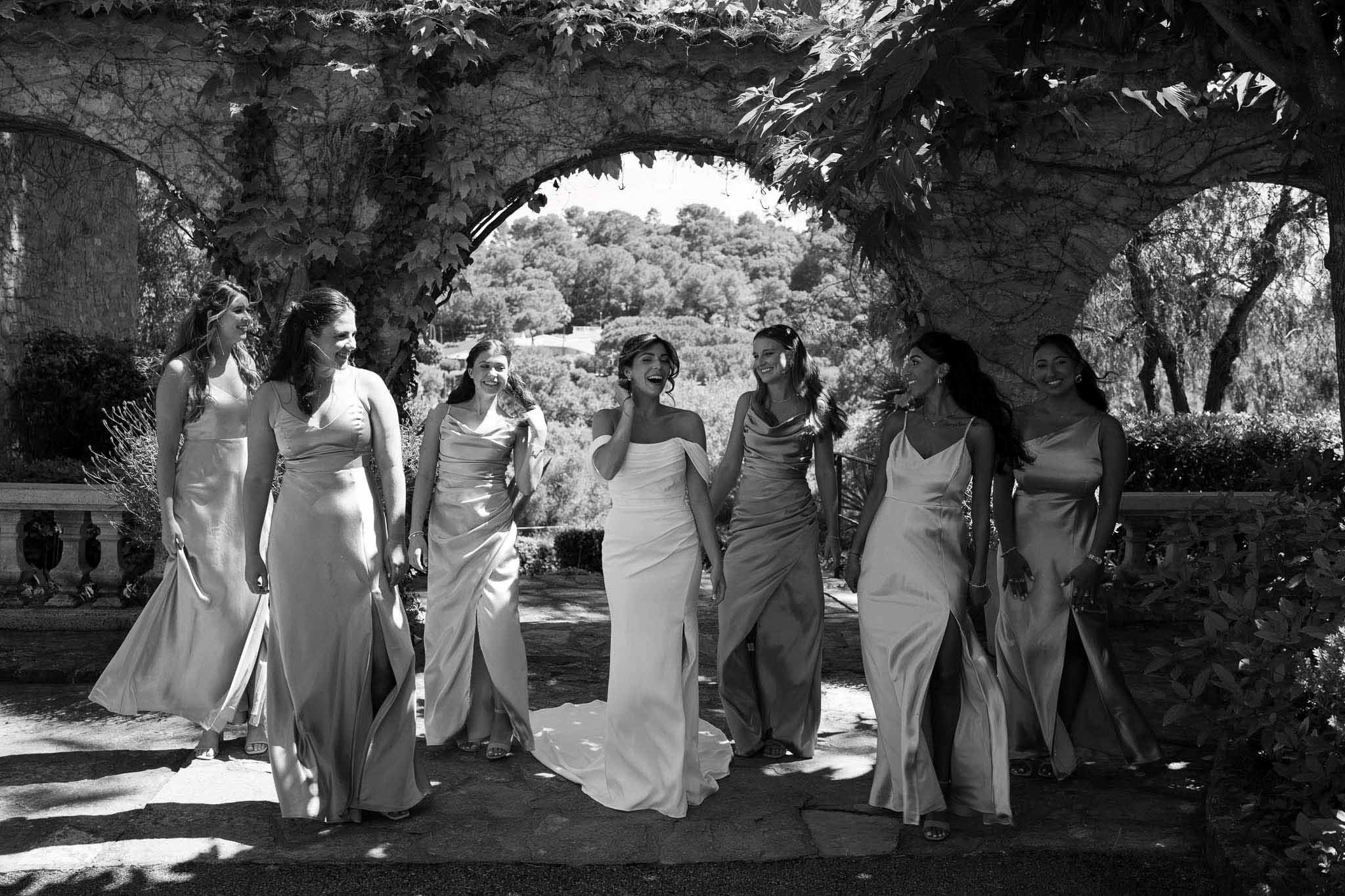 Black and white bride and six bridesmaids in satin slip dresses walking under vine-covered terrace