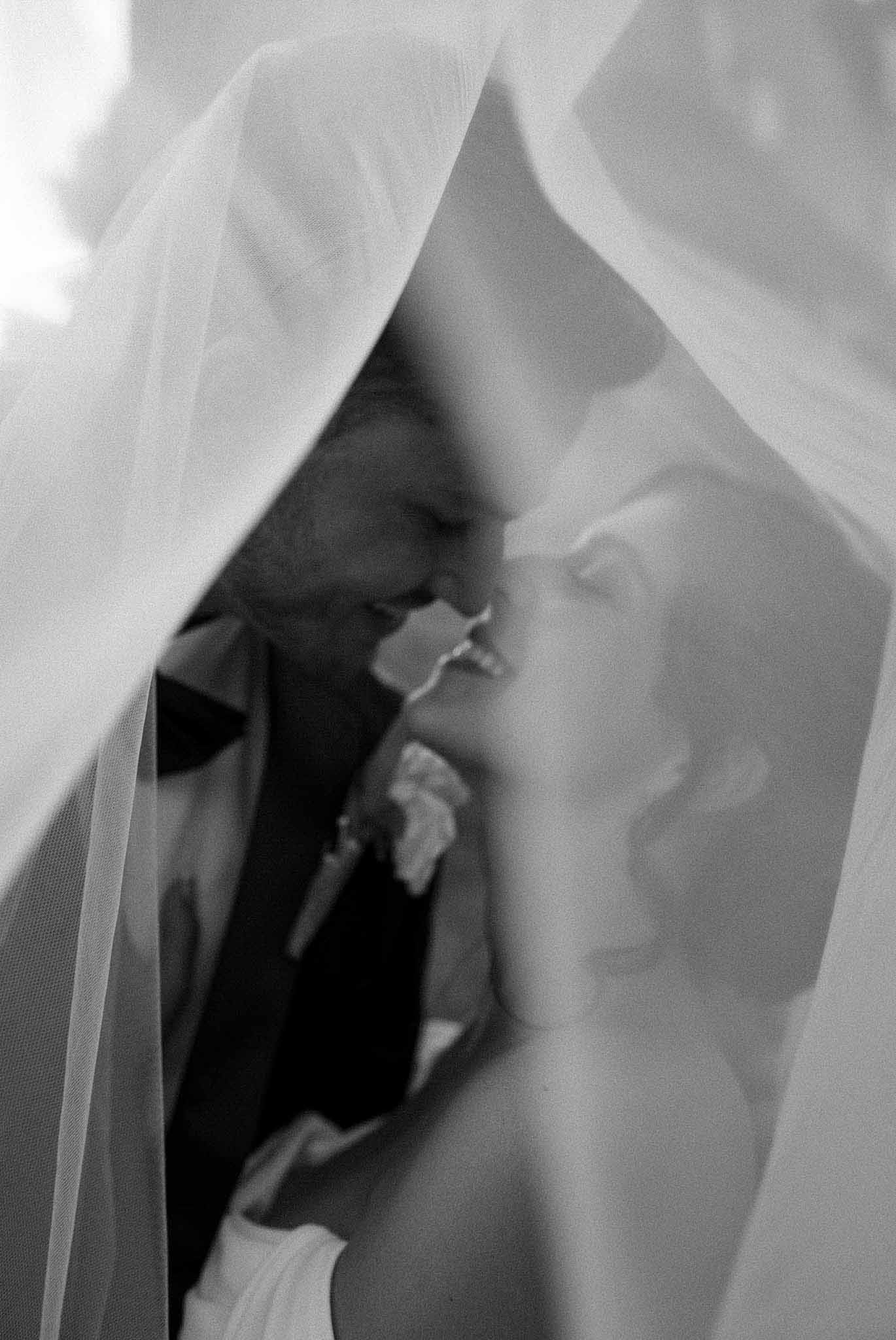 Bride and groom about to kiss framed through billowing veil in soft-focus black and white
