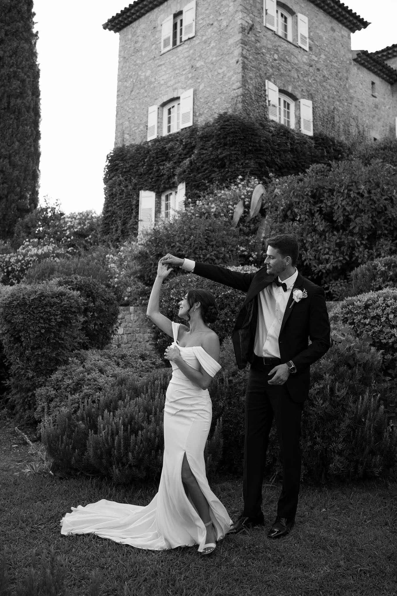 Black and white photo of bride and groom dancing in chateau garden with ivy-covered manor behind