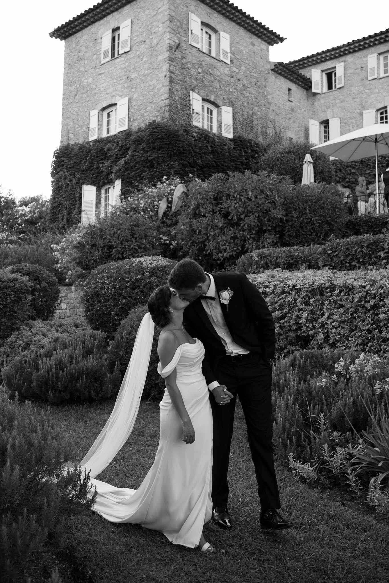 Black and white dip kiss in formal chateau garden with clipped hedges and ivy-covered facade