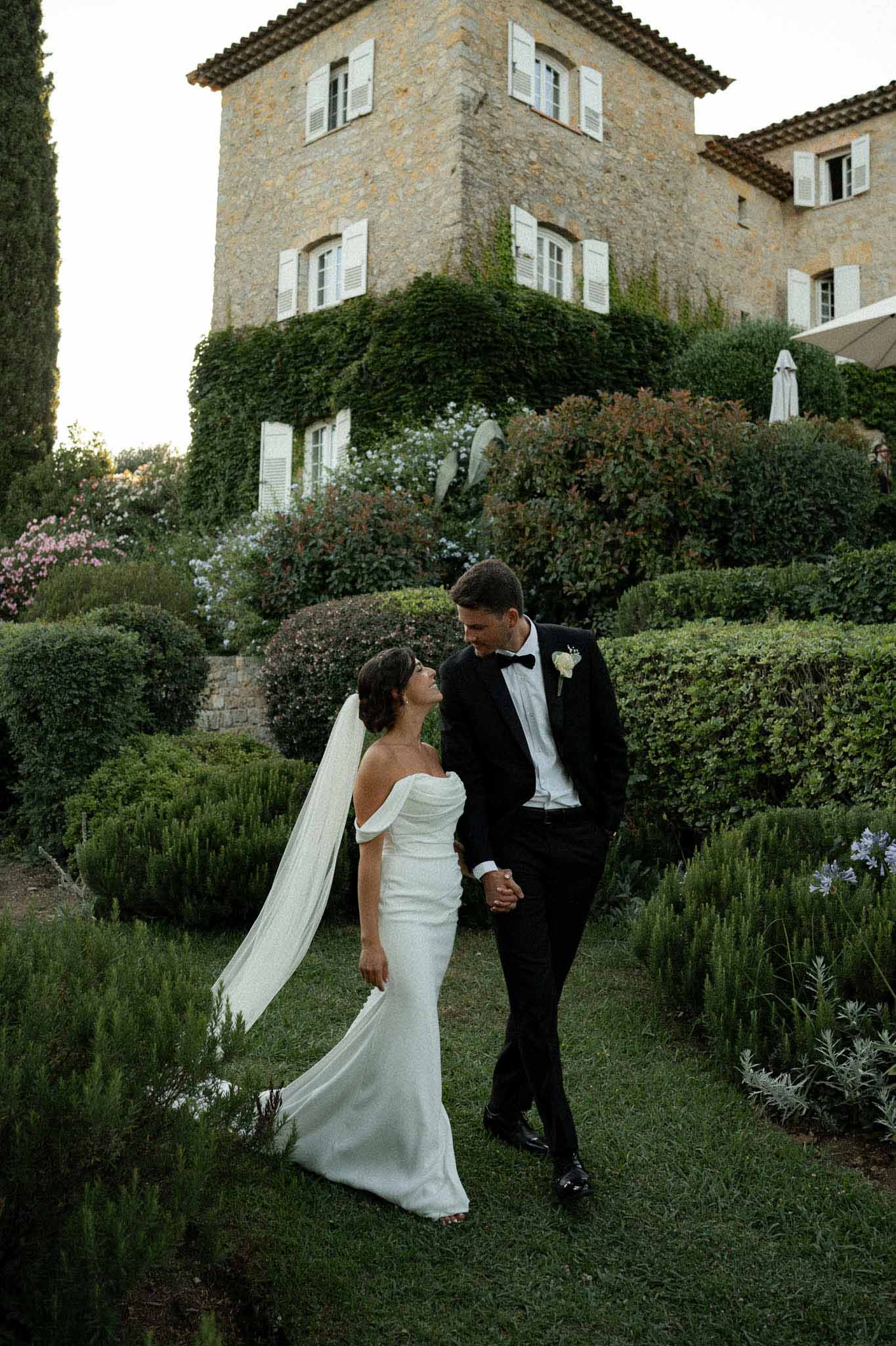 Black and white photo of bride and groom walking hand in hand in a garden