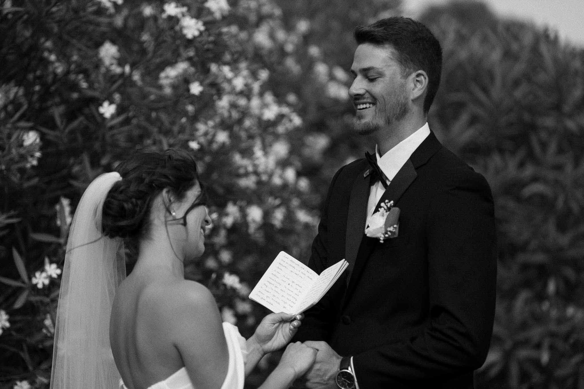 Bride reading handwritten vows to smiling groom during outdoor ceremony in black and white