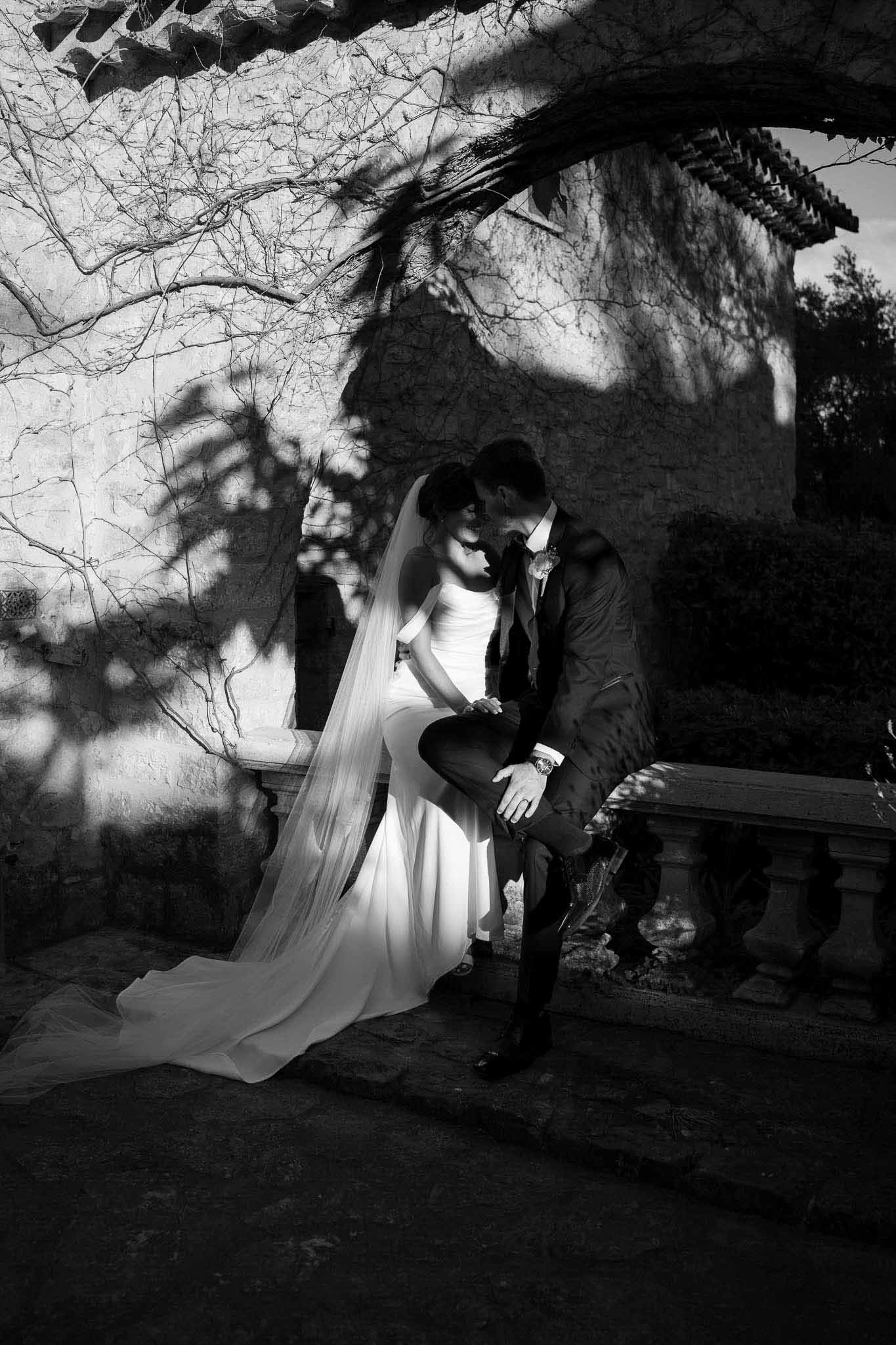Black and white couple on balustrade with cathedral veil trailing, dramatic vine shadows on stone wall