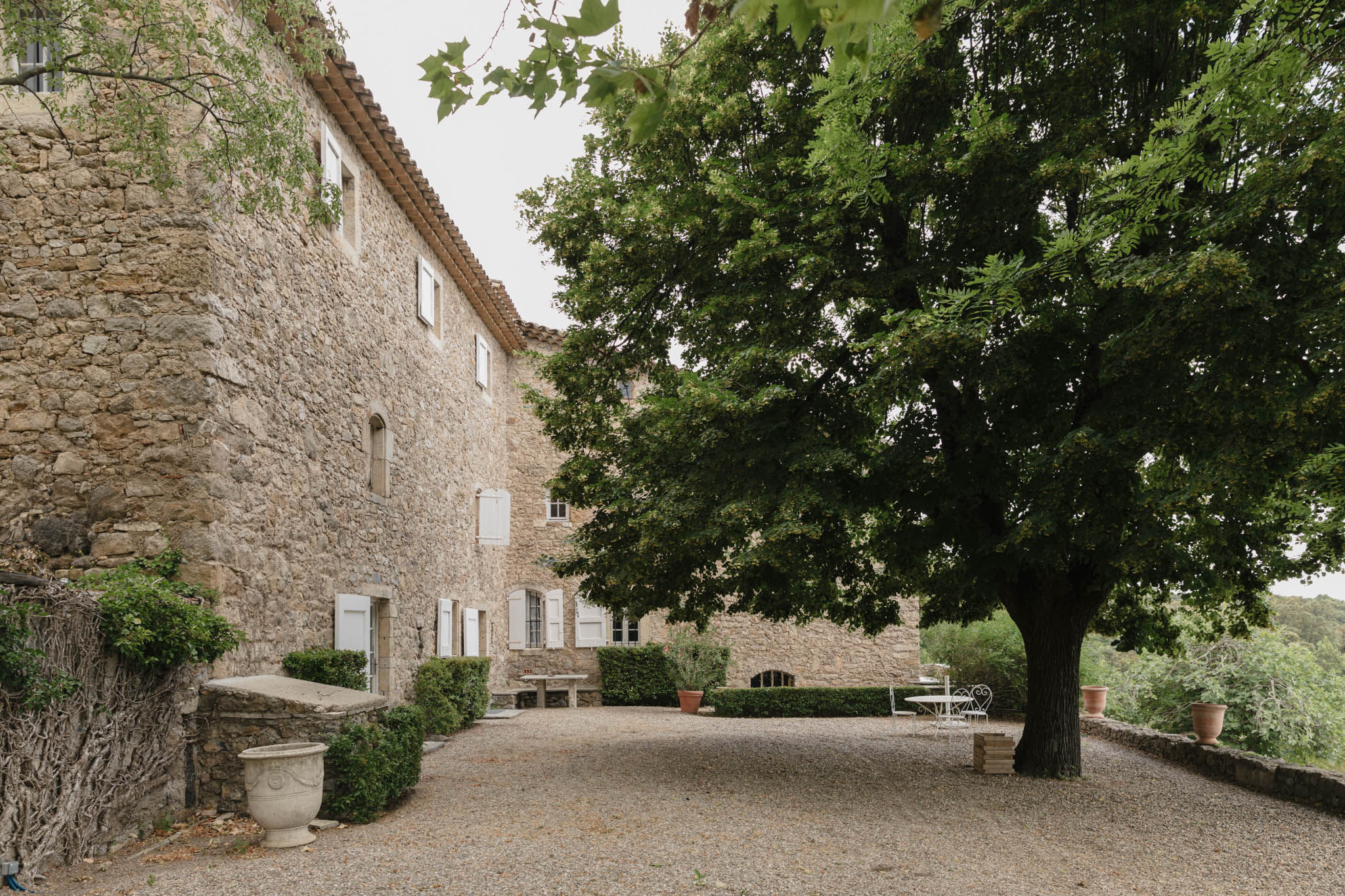 Provencal stone mas exterior with golden limestone walls, white shutters, terracotta roof, and gravel courtyard