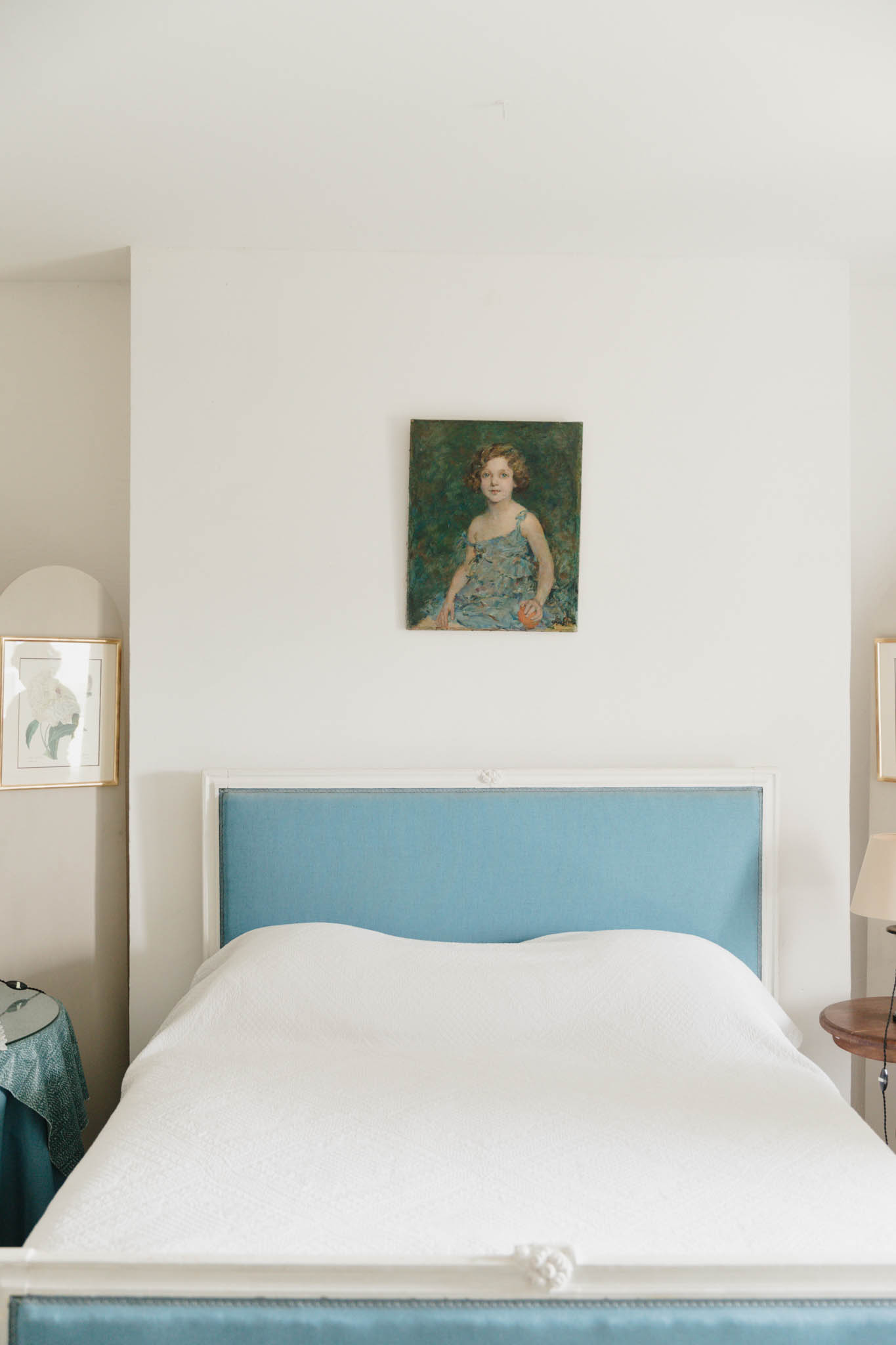 French chateau guest bedroom with powder blue upholstered bed frame, white bedspread, and antique portrait