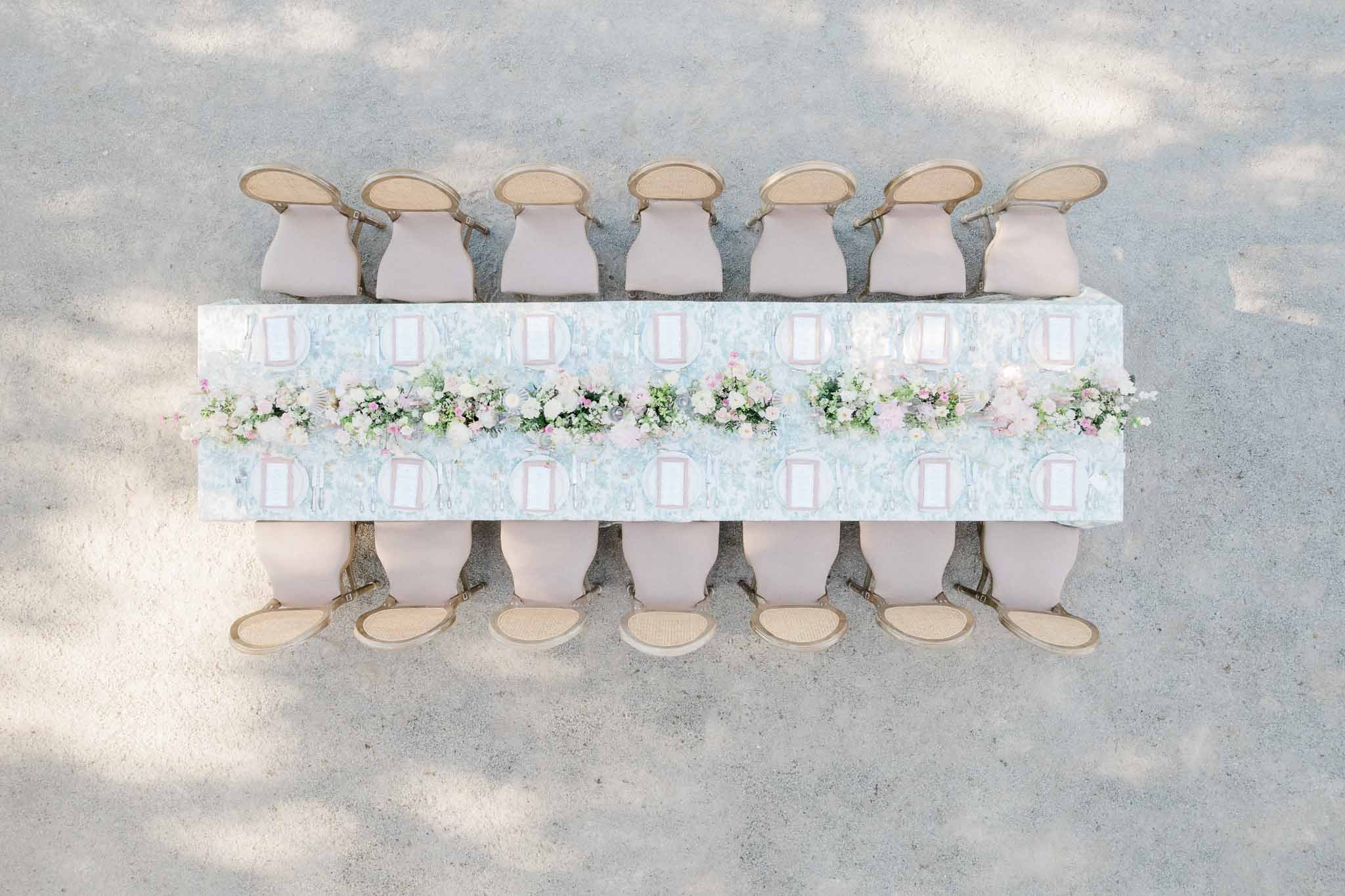 Aerial view of outdoor wedding reception table with floral runner and cream upholstered wooden chairs