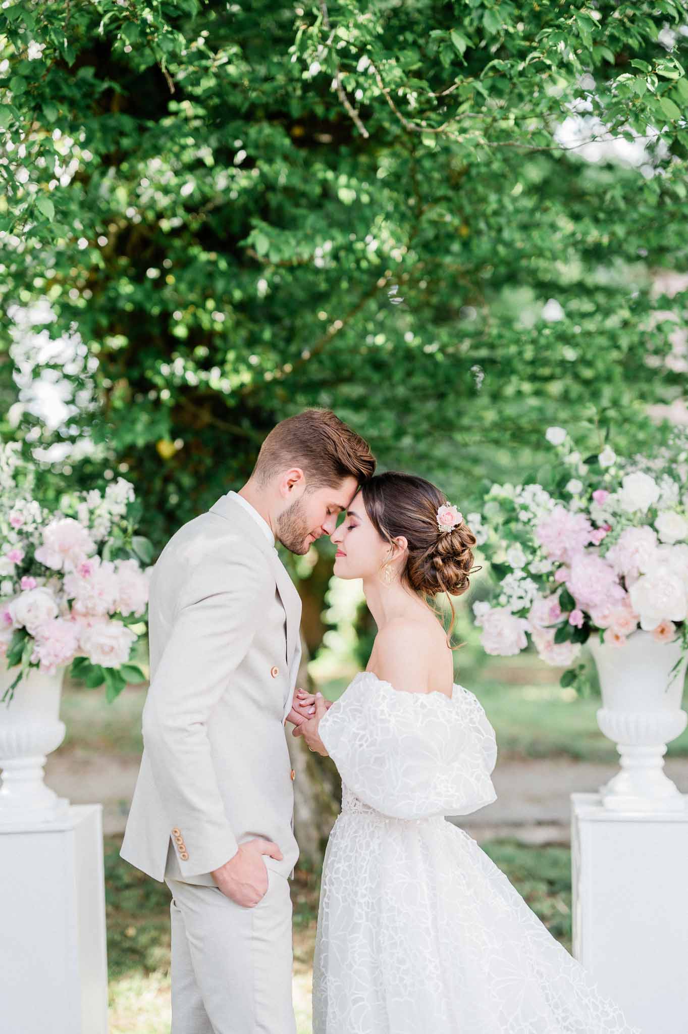 Couple sharing intimate moment during outdoor garden wedding ceremony under floral archway