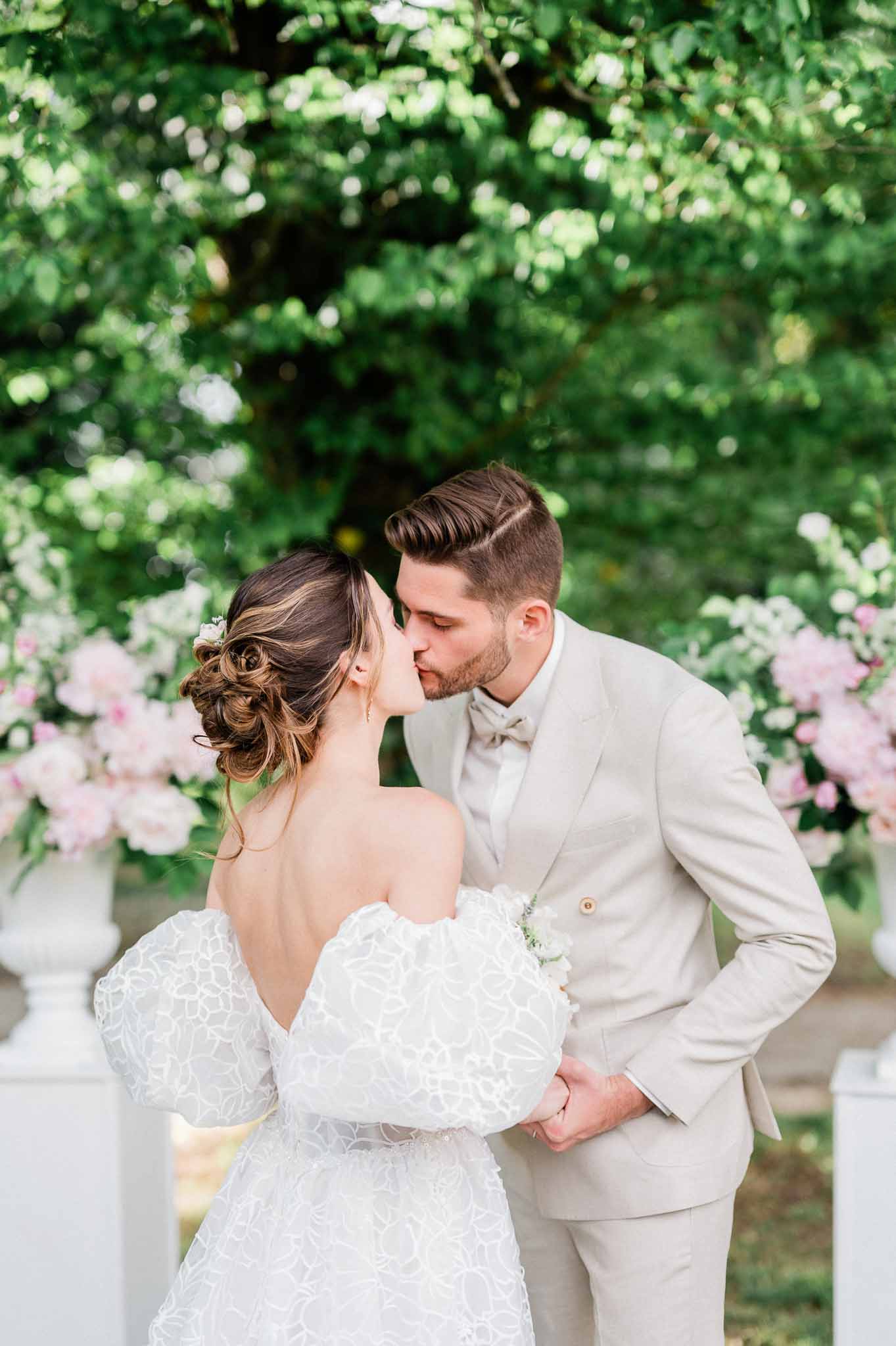Bride and groom sharing intimate kiss during garden portraits with lush hedge backdrop