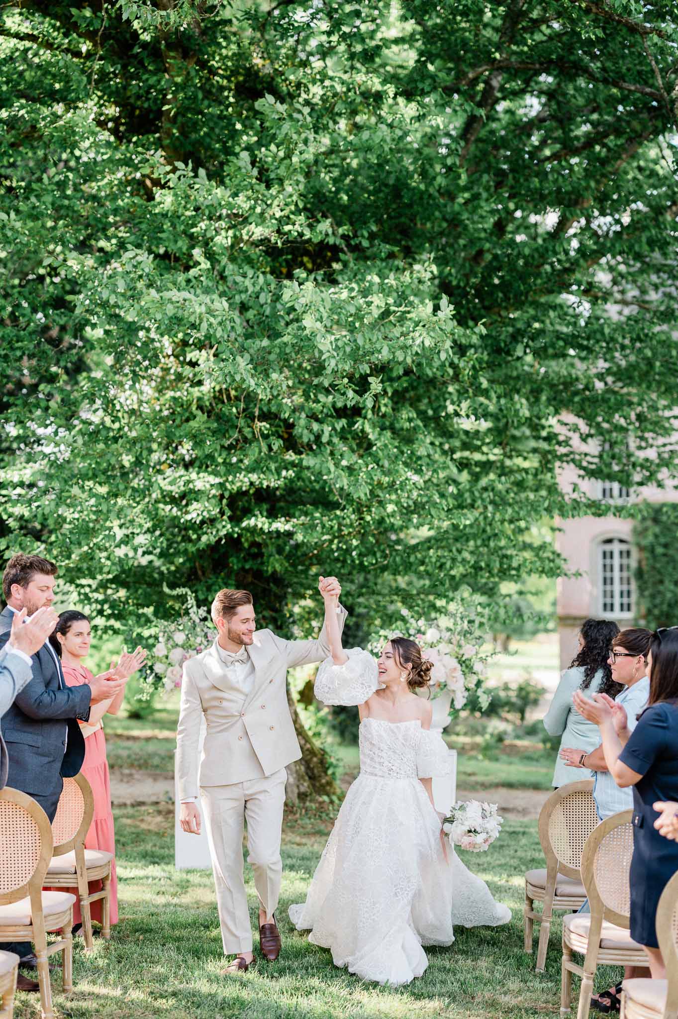 Bride and groom walking down aisle after wedding ceremony in garden setting with guests applauding