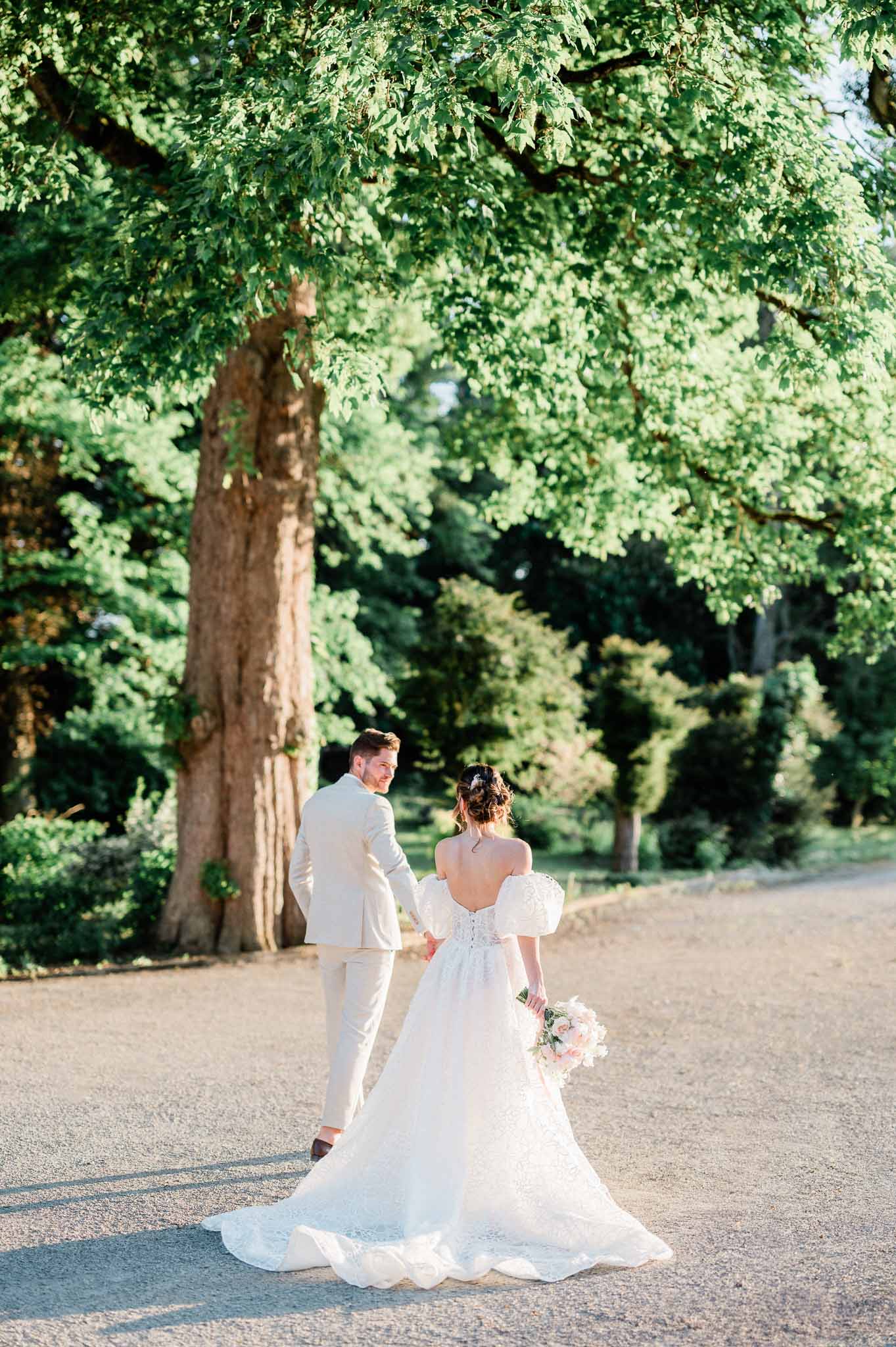Bride and groom walking down tree-lined path in formal garden setting