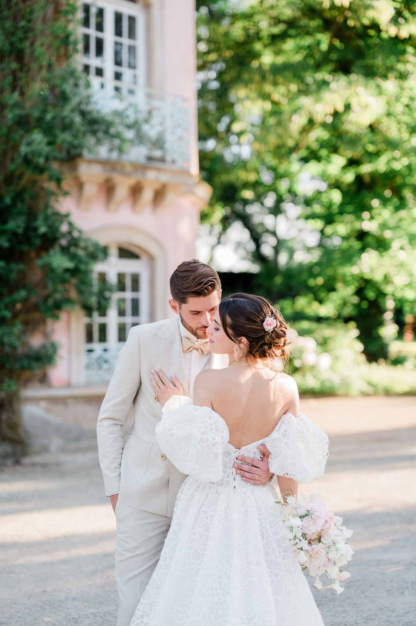 Bride and groom posing together in front of ivy-covered stone building in garden courtyard setting