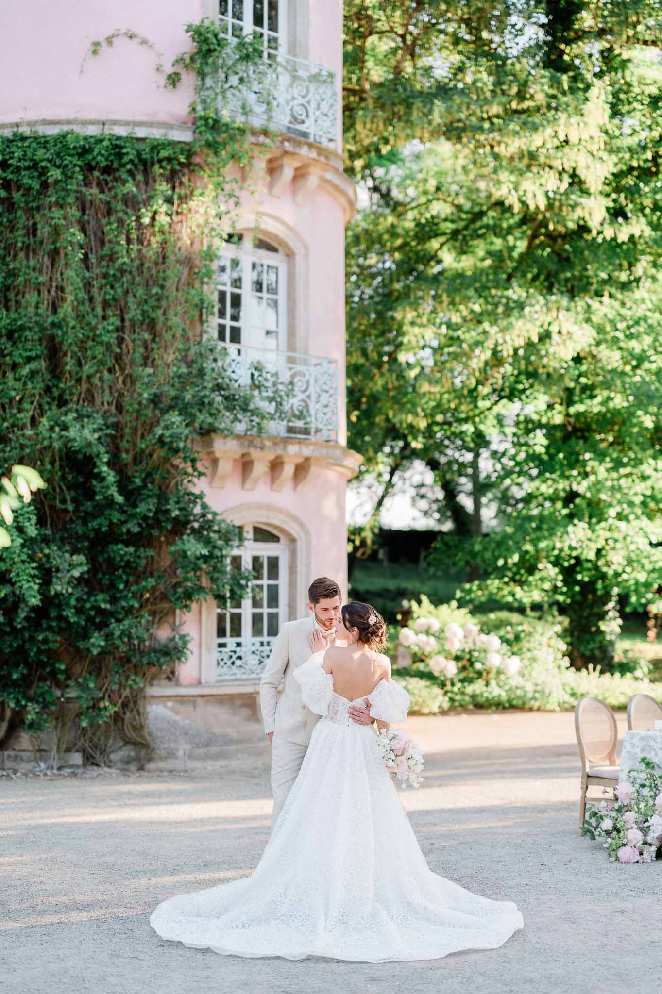 Bride and groom portrait in pink stone château courtyard with ivy-covered walls and manicured gardens