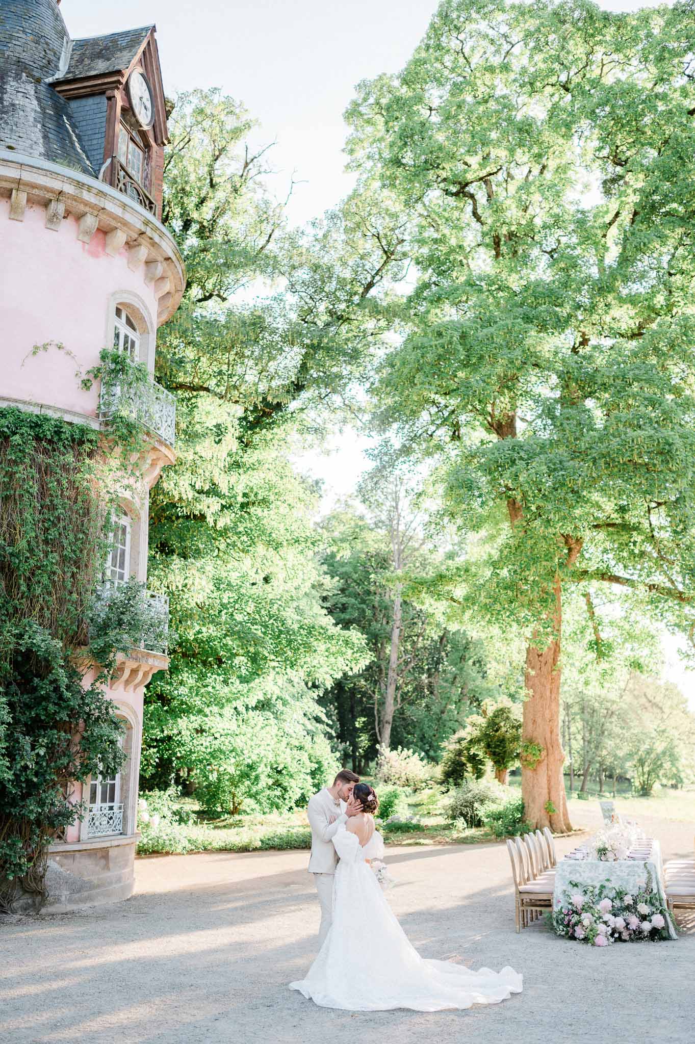 Bride and groom embrace in tree-lined château courtyard during outdoor wedding reception