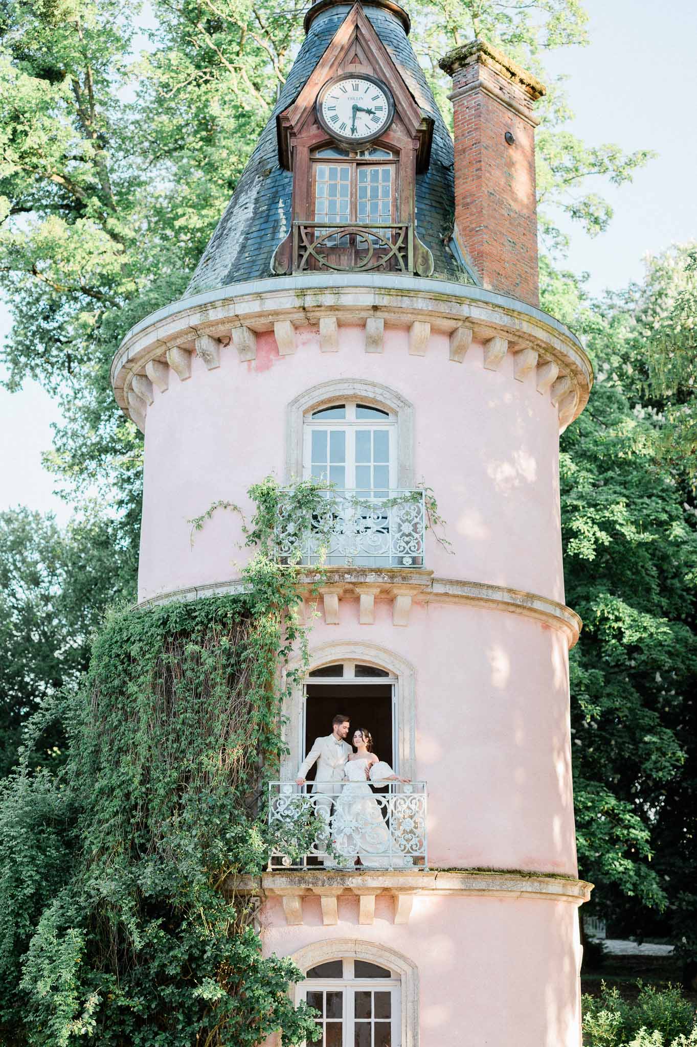 Bride and groom posing on balcony of historic pink tower with clock at wedding venue