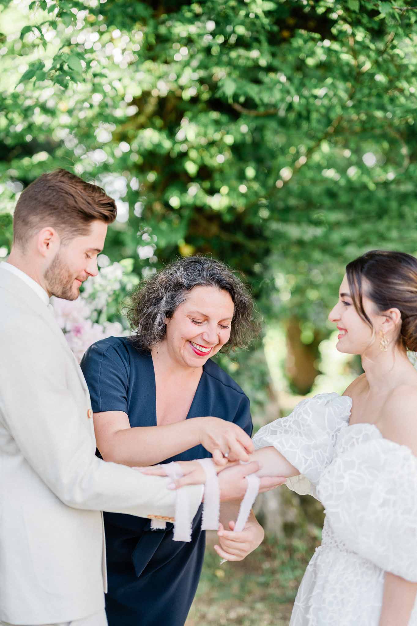 Handfasting ceremony with officiant binding couple's hands with white ribbon in garden setting