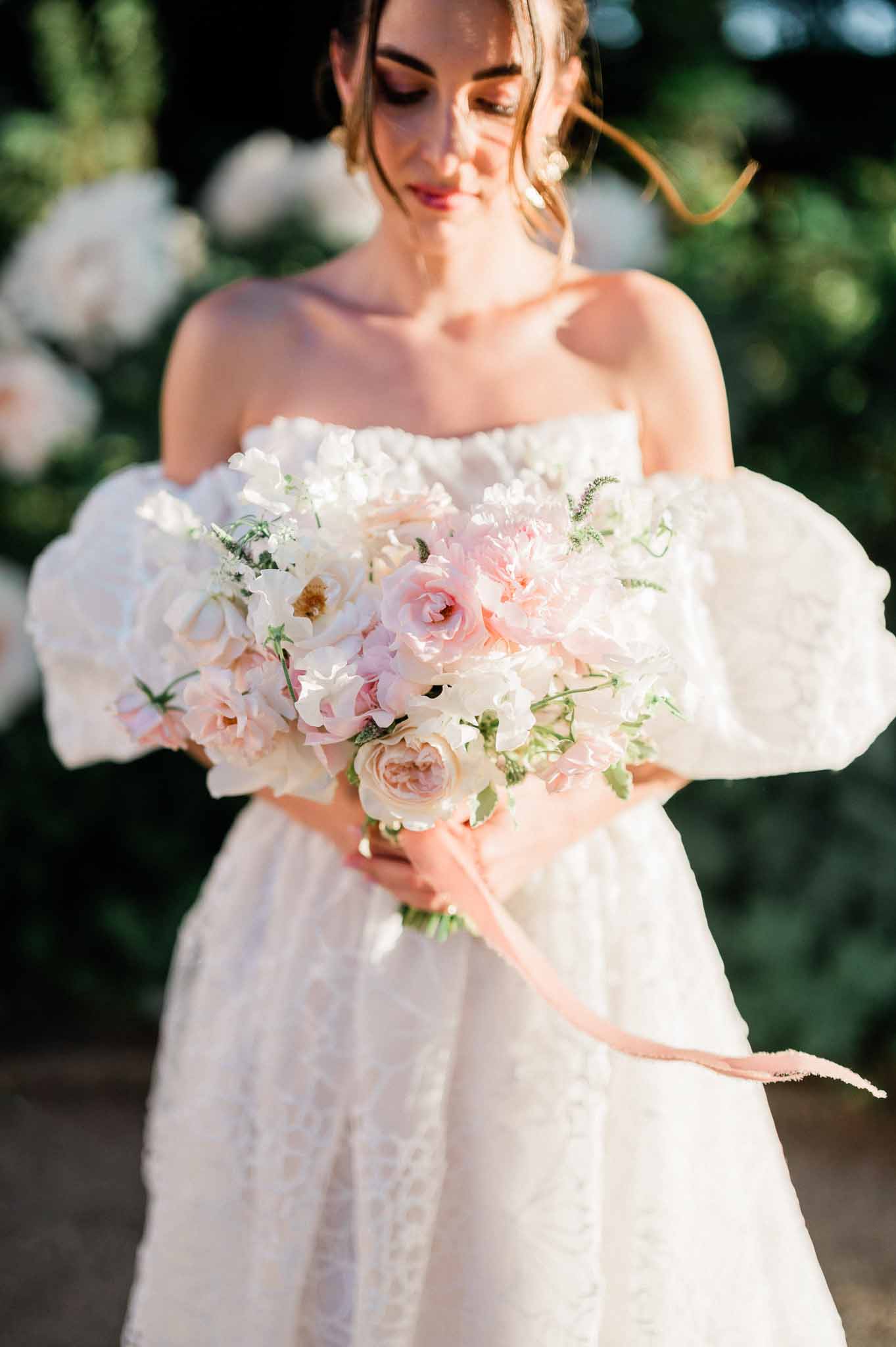 Bride holding bridal bouquet in garden setting wearing ivory off-shoulder wedding dress