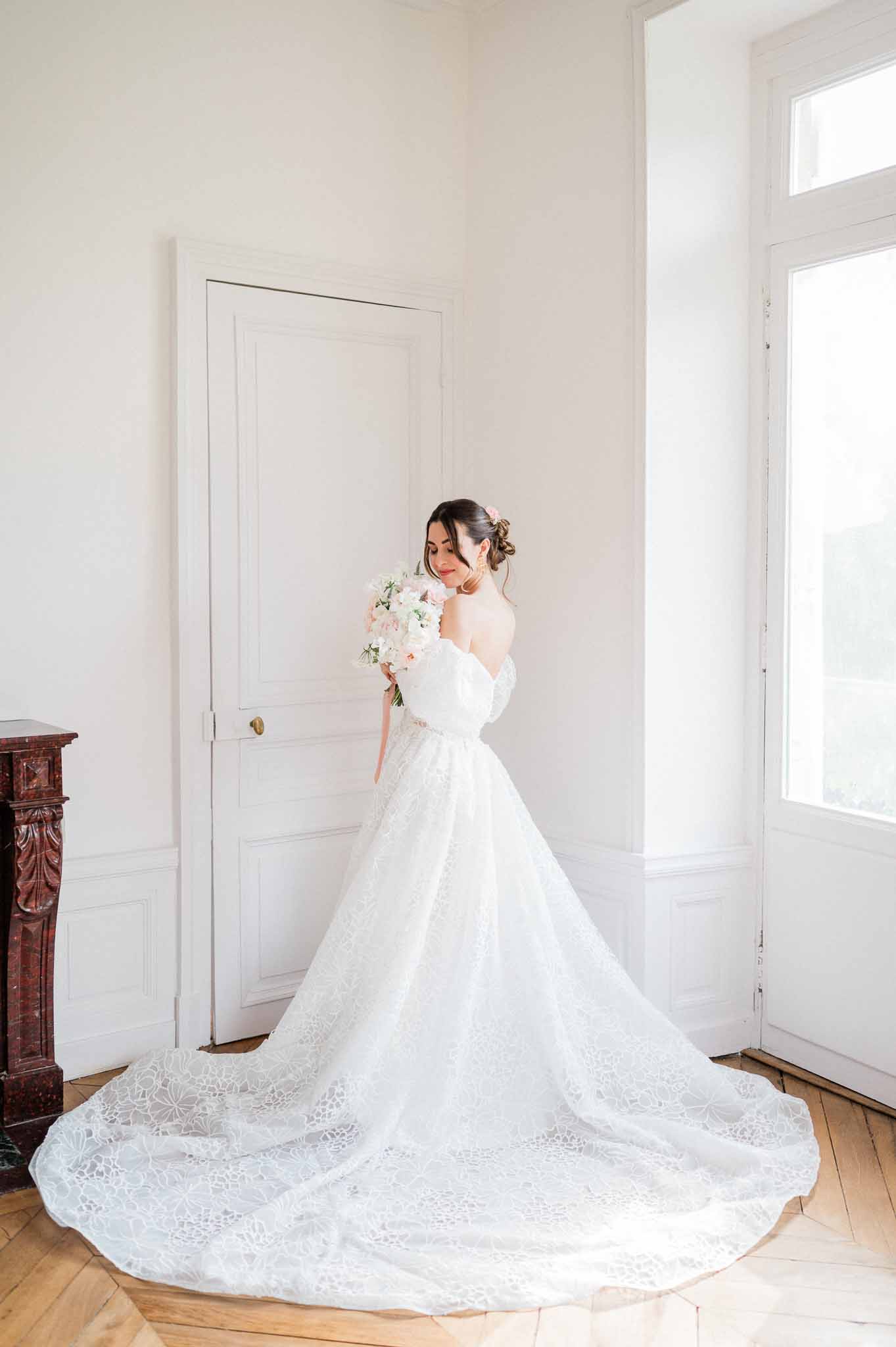 Bride in ivory lace cathedral train dress holding blush bouquet in bright minimalist interior room
