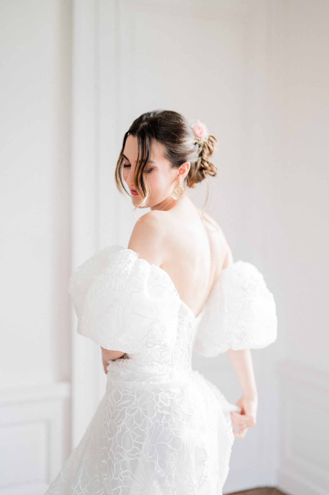 Bride in ivory off-shoulder dress with beaded details and low braided bun indoors