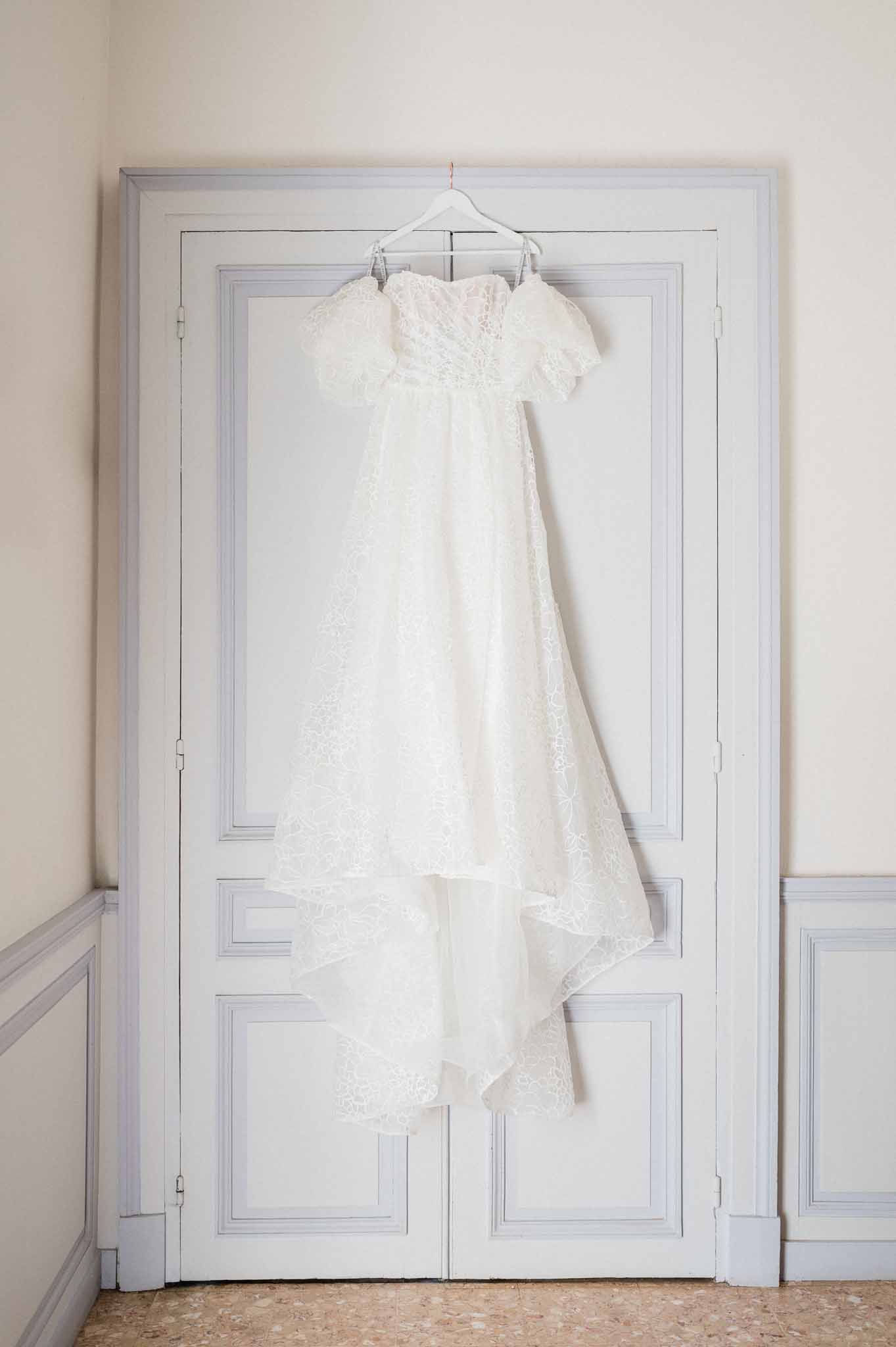 Ivory lace wedding dress hanging on white door before ceremony