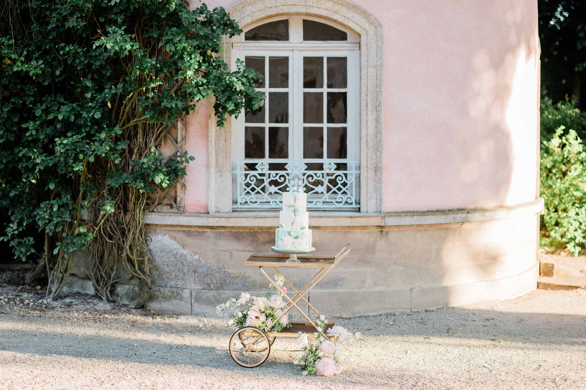 White wedding cake with gold accents and blush floral display at historic stone courtyard venue