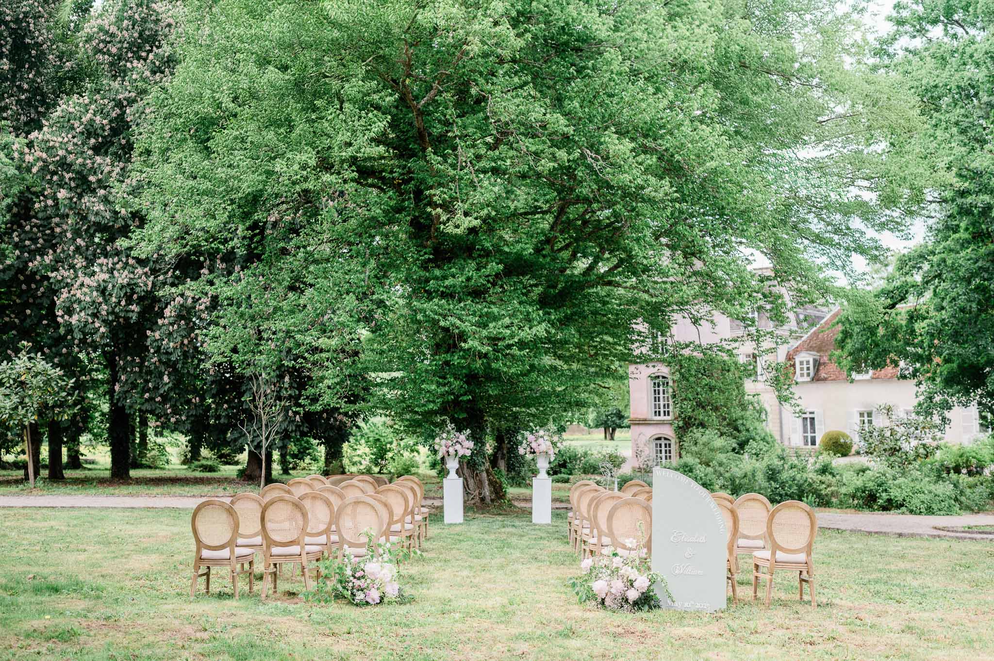 Outdoor wedding ceremony setup in manicured garden with manor house backdrop
