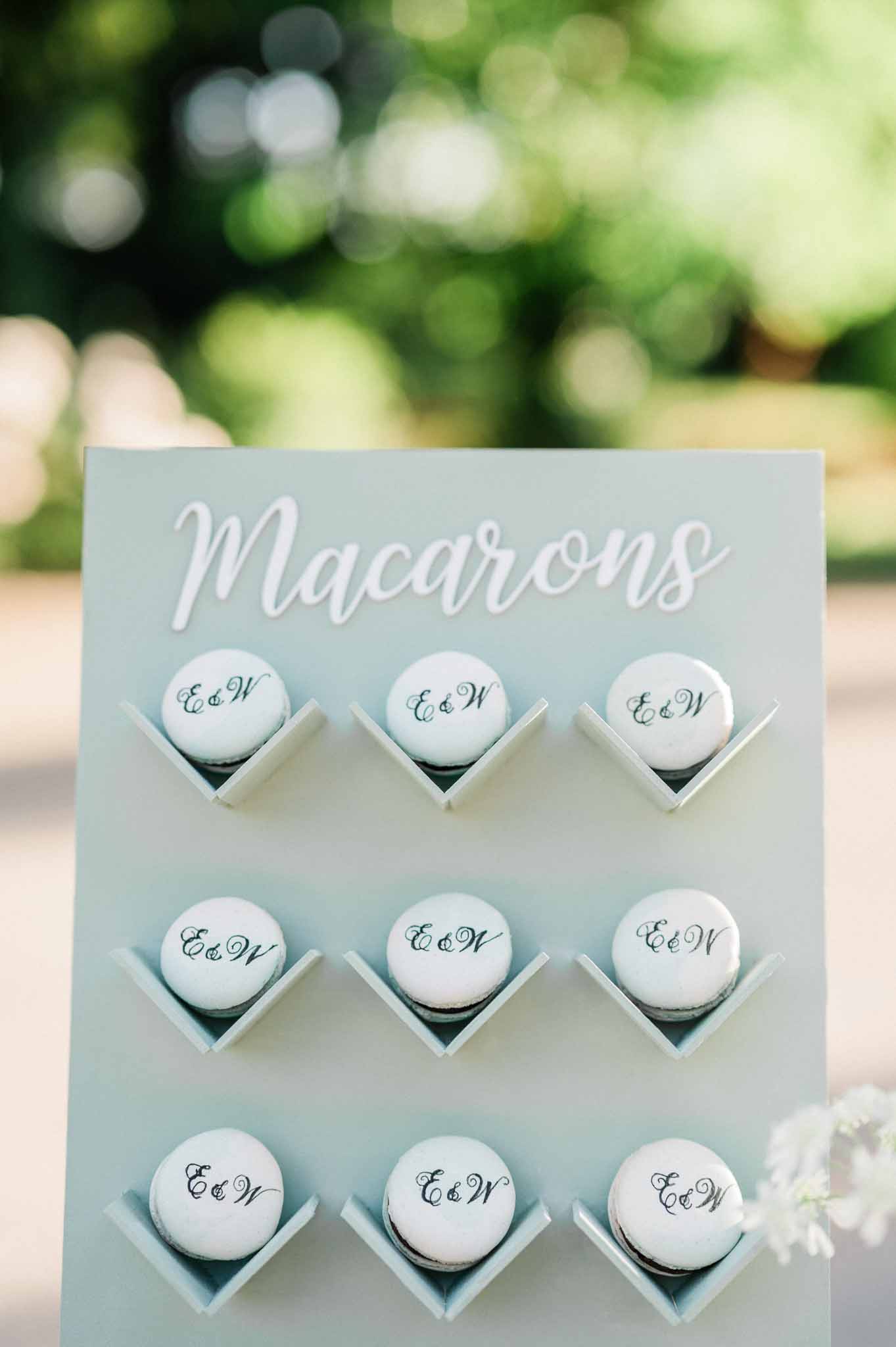 Personalized wedding macarons with initials E & W displayed on pale blue card in outdoor garden setting
