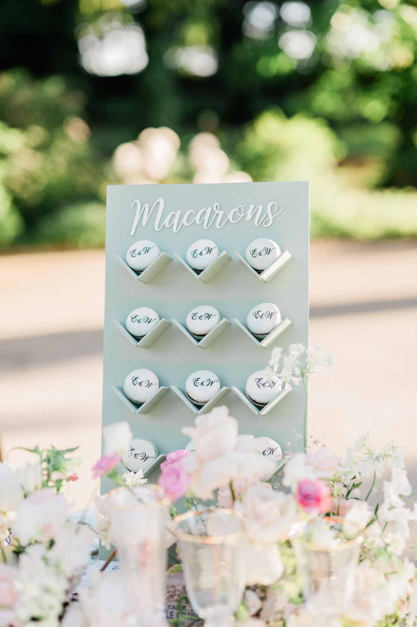 Monogrammed macaron wedding favor display with pale blue sign in garden setting