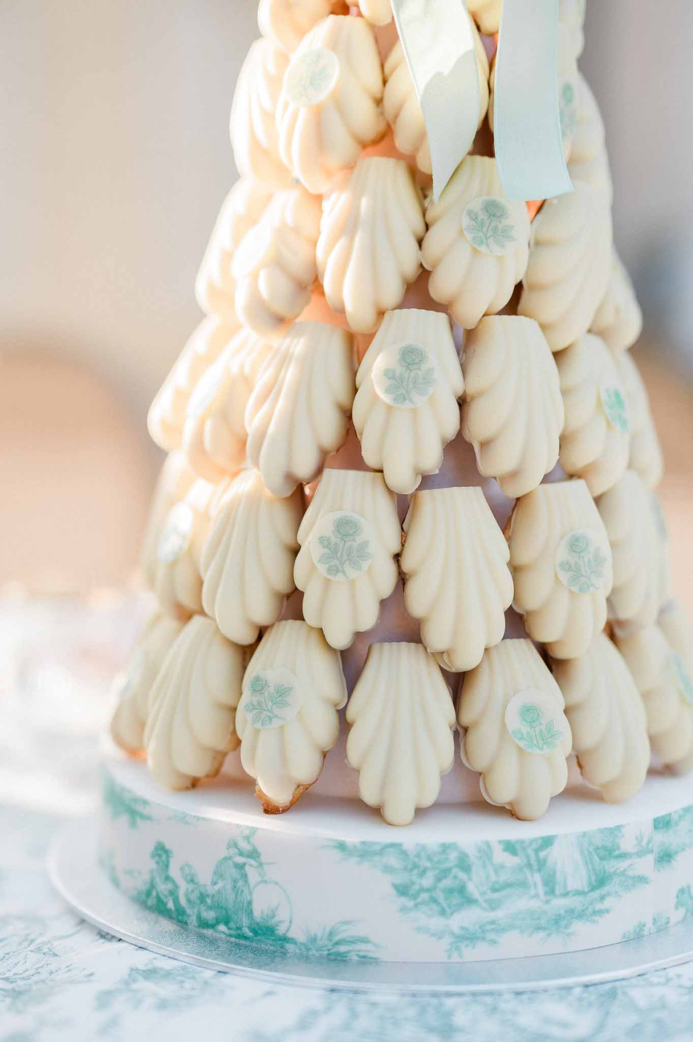 Croquembouche tower with sage green leaf decorations and blue ribbons at wedding reception