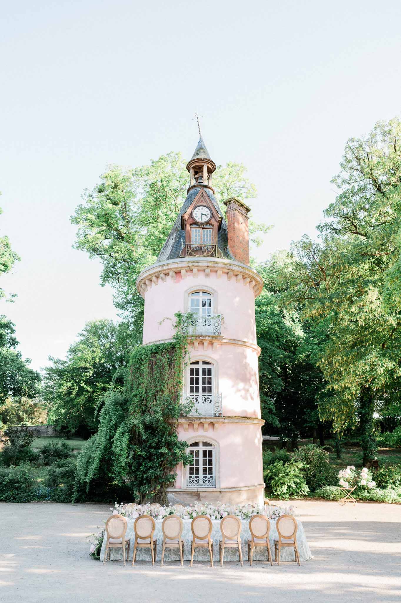 Ceremony setup with wooden chairs and white florals in front of pink tower at château courtyard