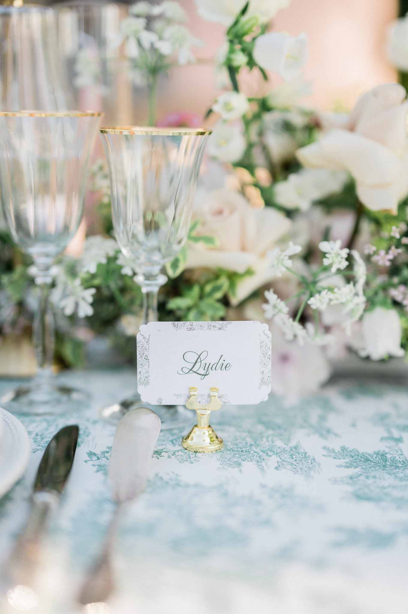 Reception table setting with gold place card holder and crystal glasses at garden wedding