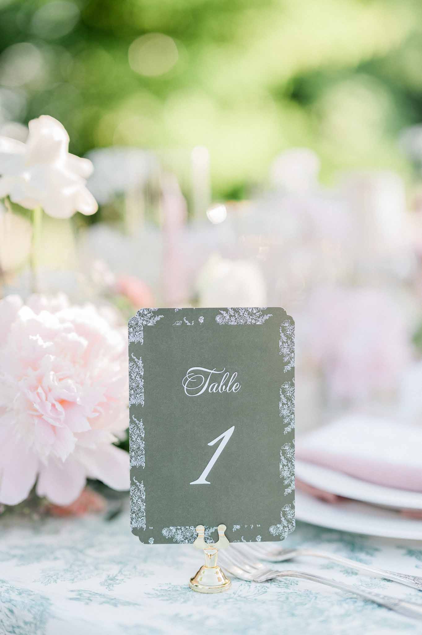 Sage green table number card with pink peonies and white flowers at garden reception table setting