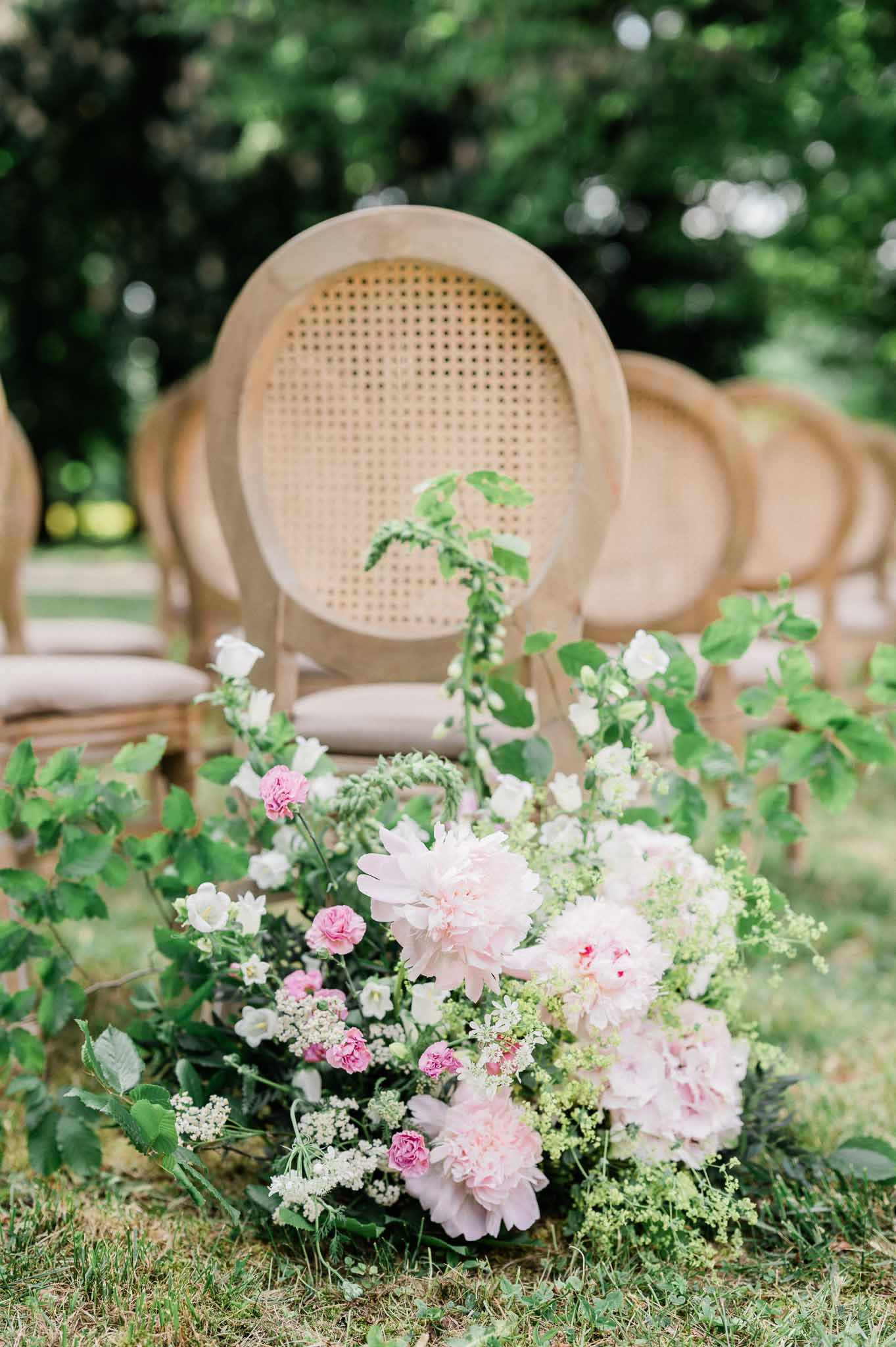 Rattan ceremony chairs with pink and white floral arrangements at outdoor garden wedding