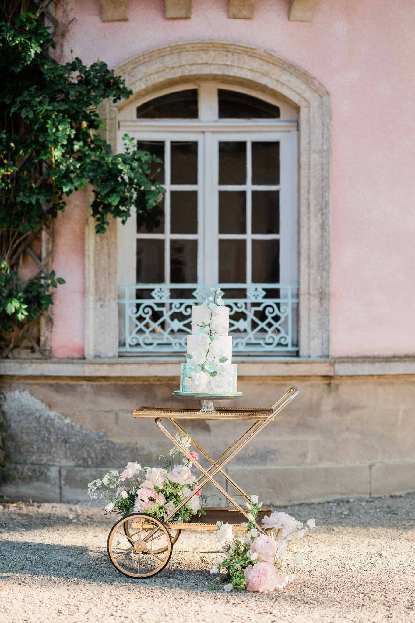 Two-tiered wedding cake with botanical details on gold stand in courtyard setting