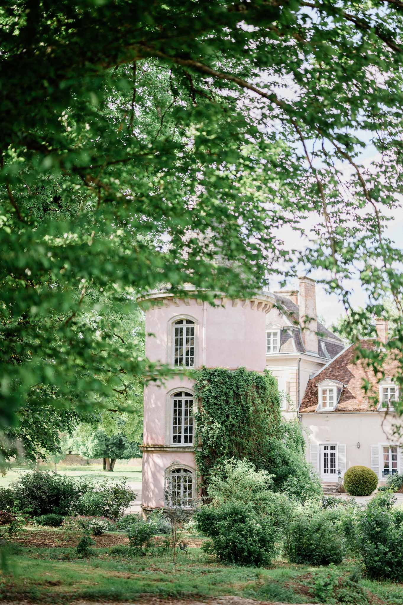 French estate building with blush tower and ivy-covered walls framed by tree branches