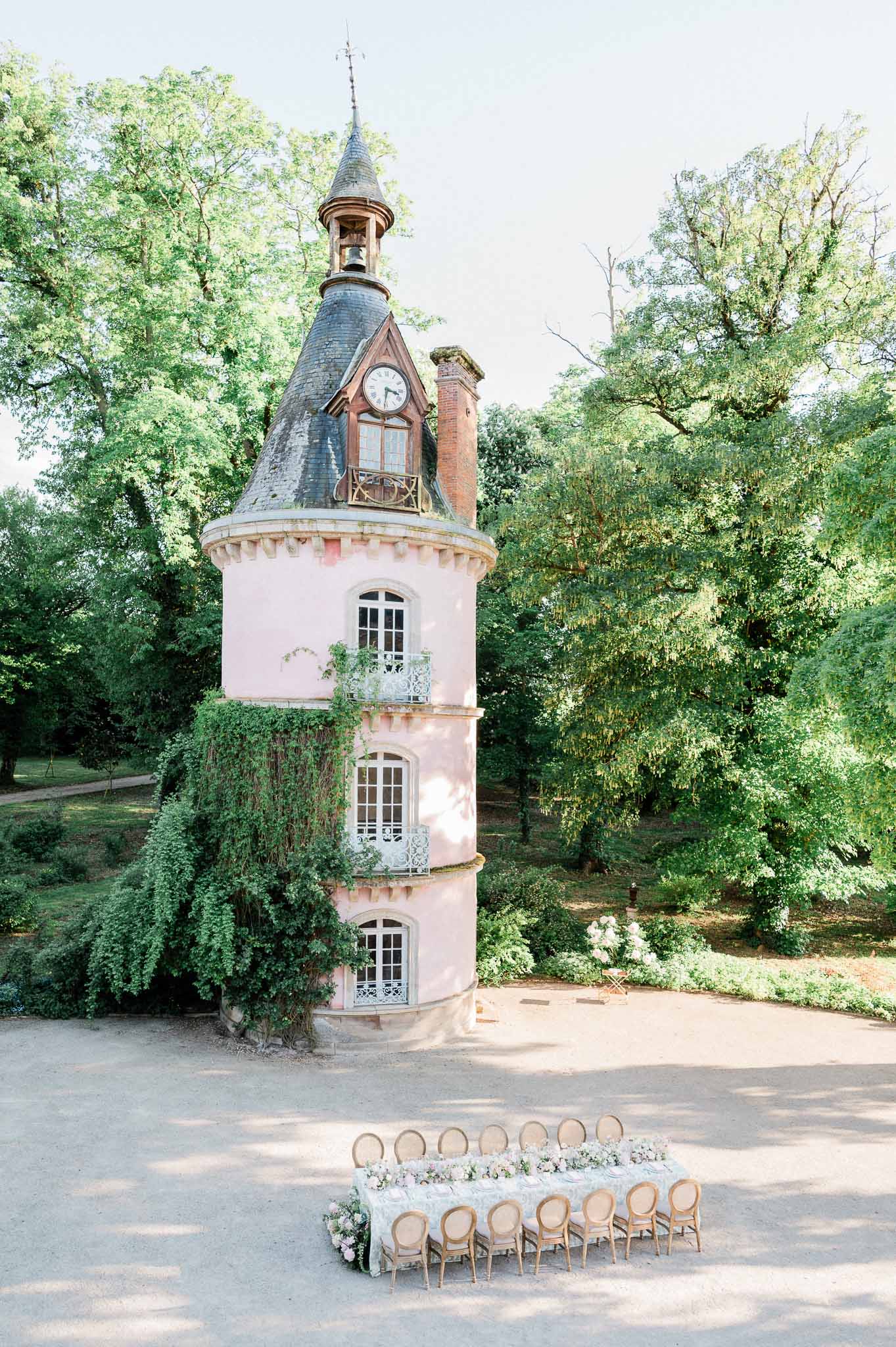 Outdoor wedding ceremony setup with wooden chairs and florals in front of historic pink tower