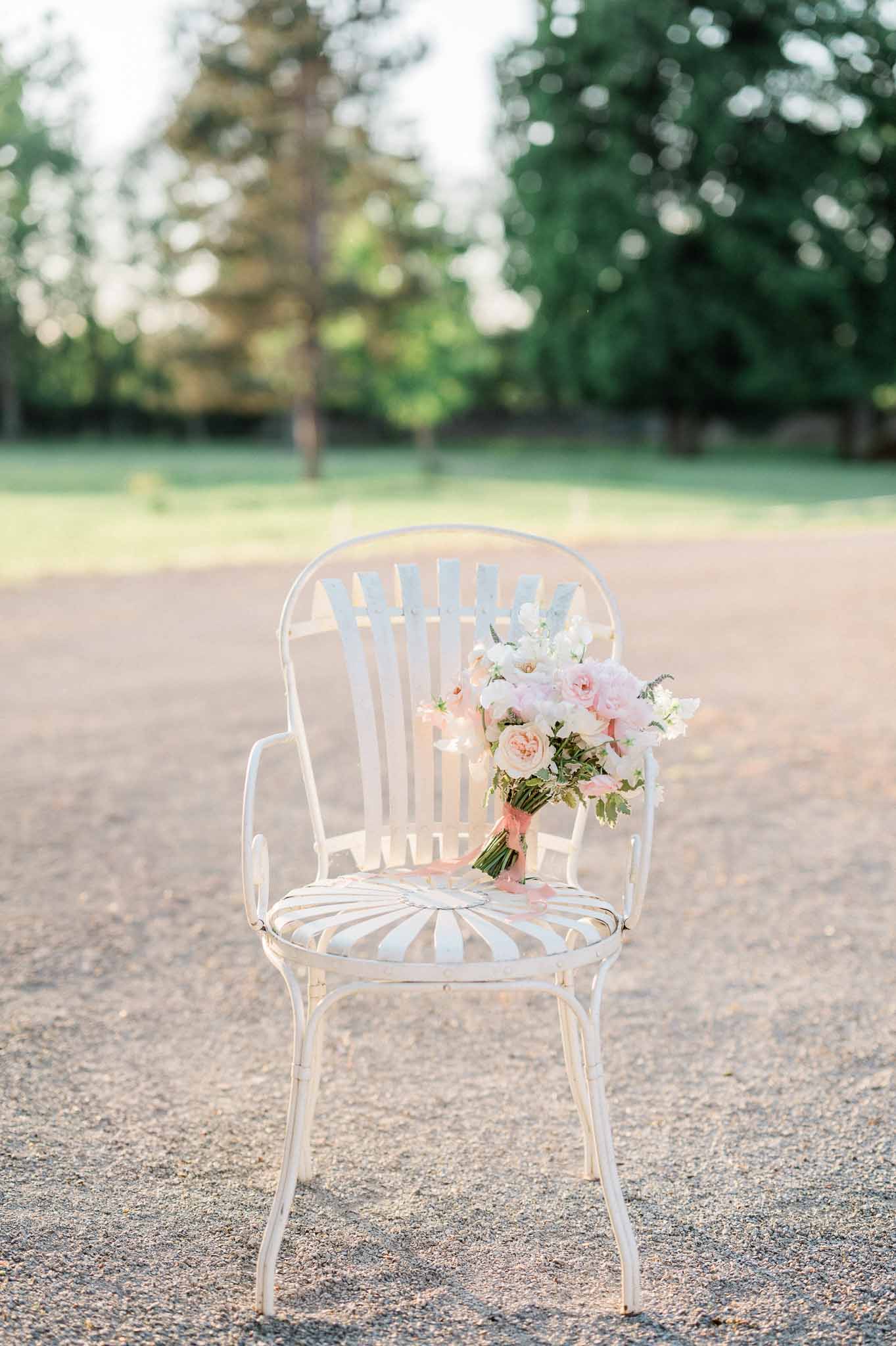 Bridal bouquet with blush roses and white peonies displayed on bentwood chair in garden setting