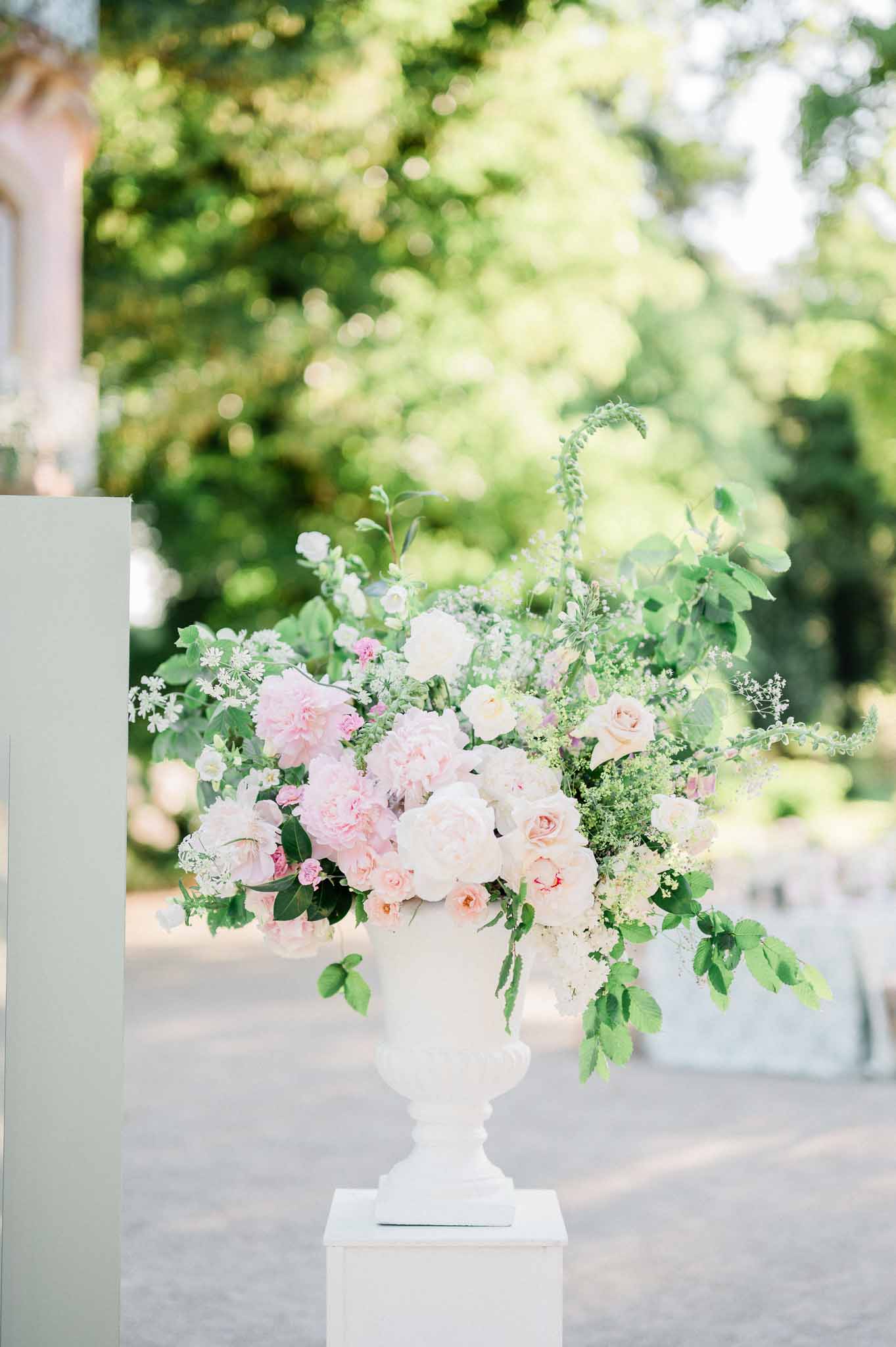 Pink and white floral centerpiece in white urn at garden wedding venue