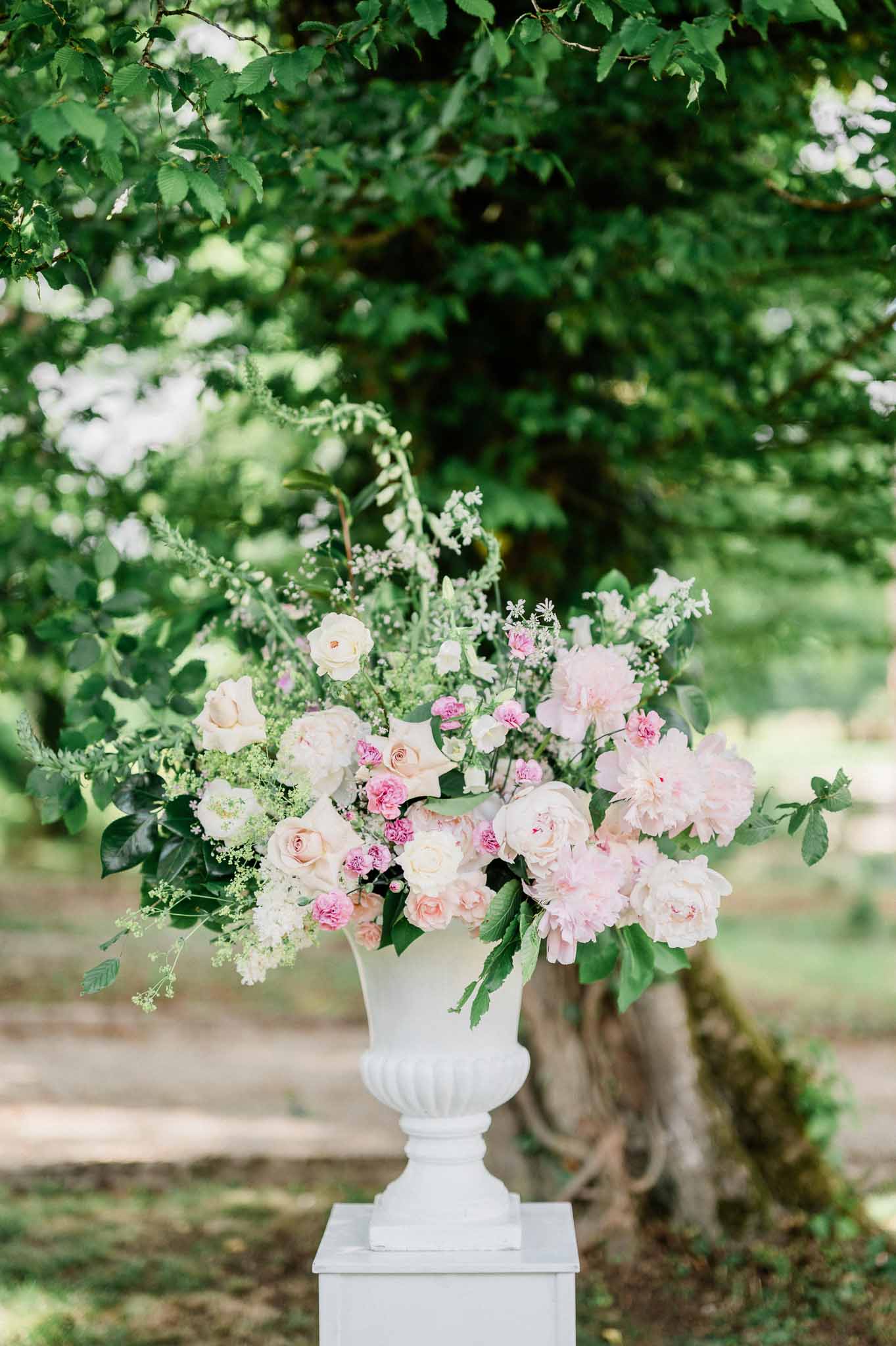Floral arrangement in white urn vase with pink roses and greenery in garden setting